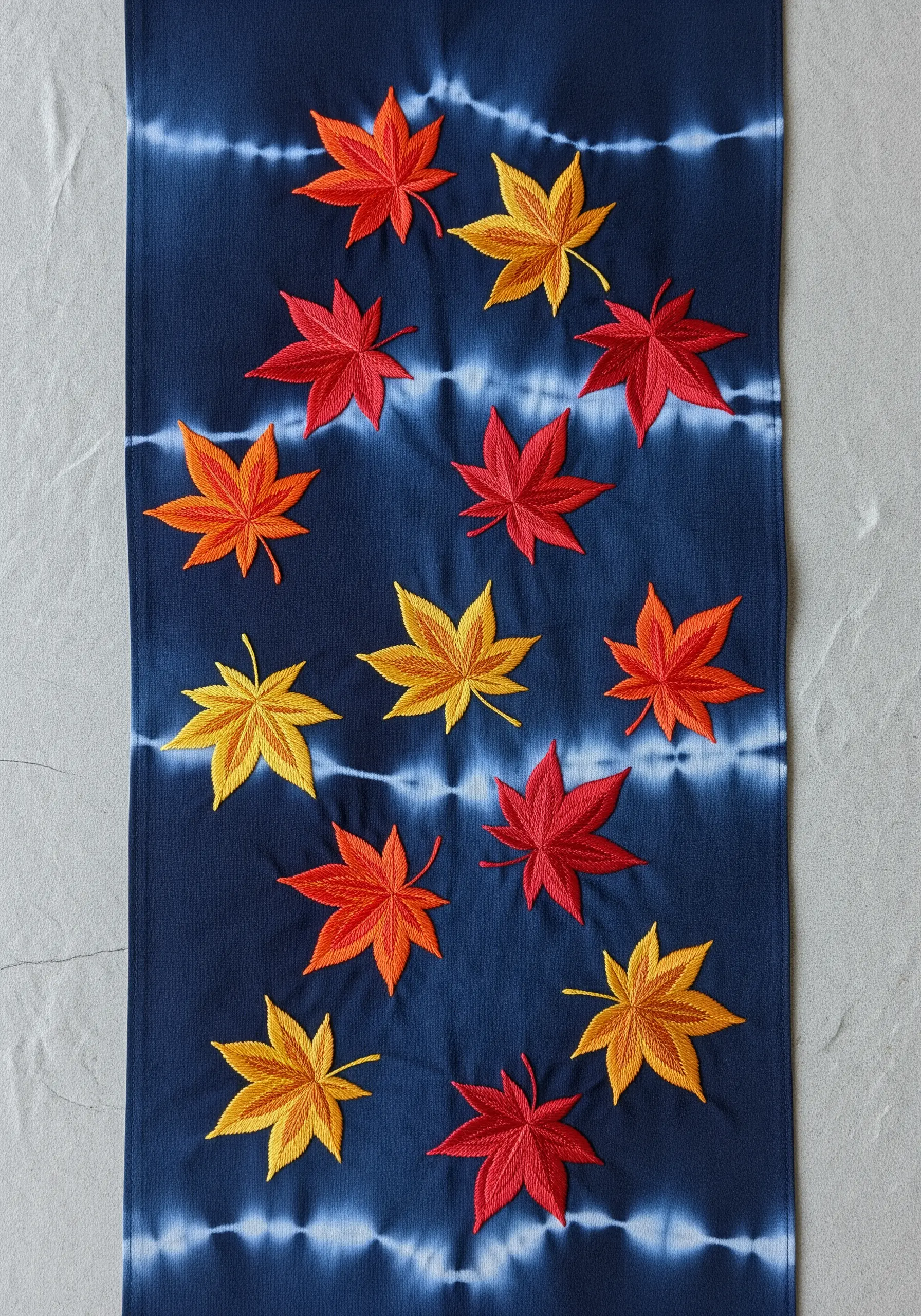 Embroidered Japanese maple leaves in red, orange, and yellow on an indigo shibori-dyed runner.