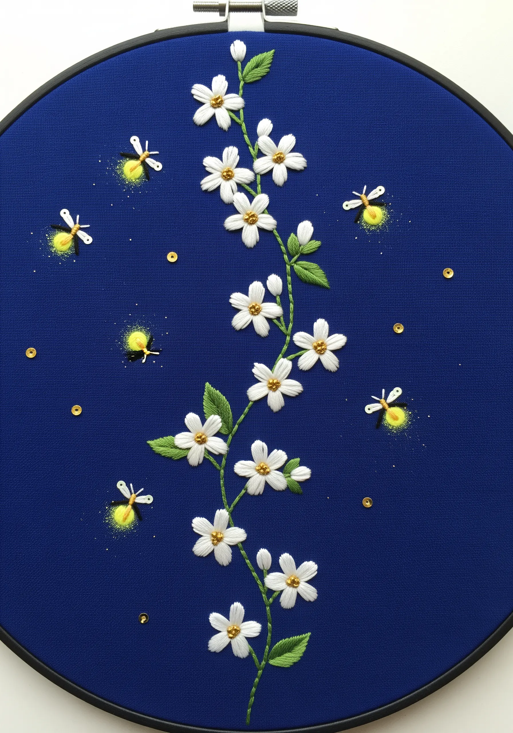 Embroidery of a white jasmine vine surrounded by glowing fireflies on a royal blue background.