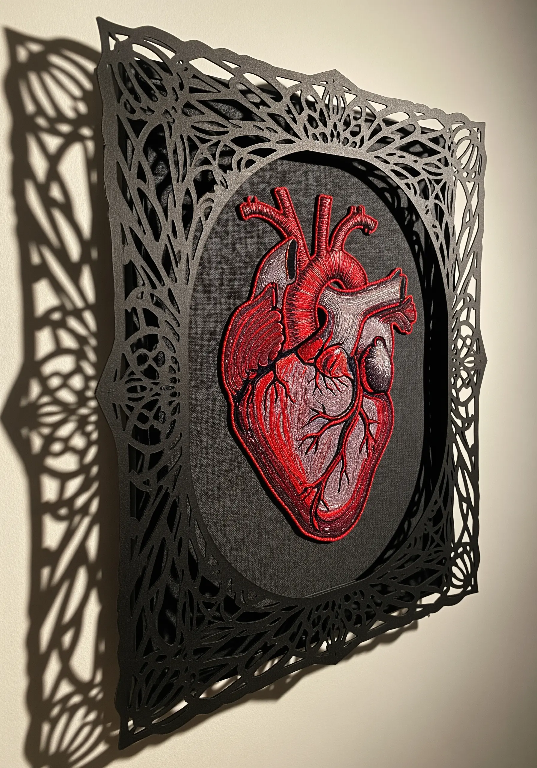 Embroidered anatomical heart framed by an intricate, black laser-cut paper design.