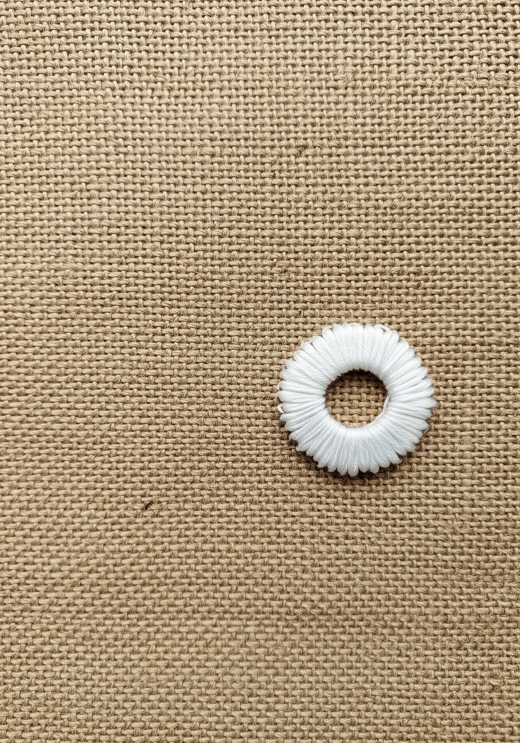 A single, smooth white satin stitch circle on a rough, textured burlap background.