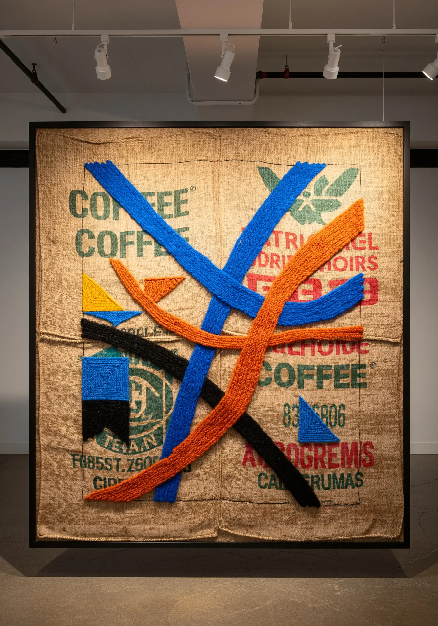 An old burlap coffee sack is stretched in a frame and embellished with abstract shapes in chunky yarn.