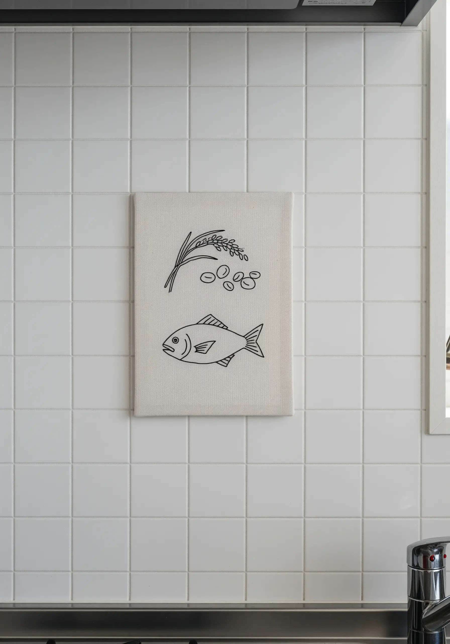 A simple line embroidery of rice, beans, and a fish on a tiled kitchen wall.