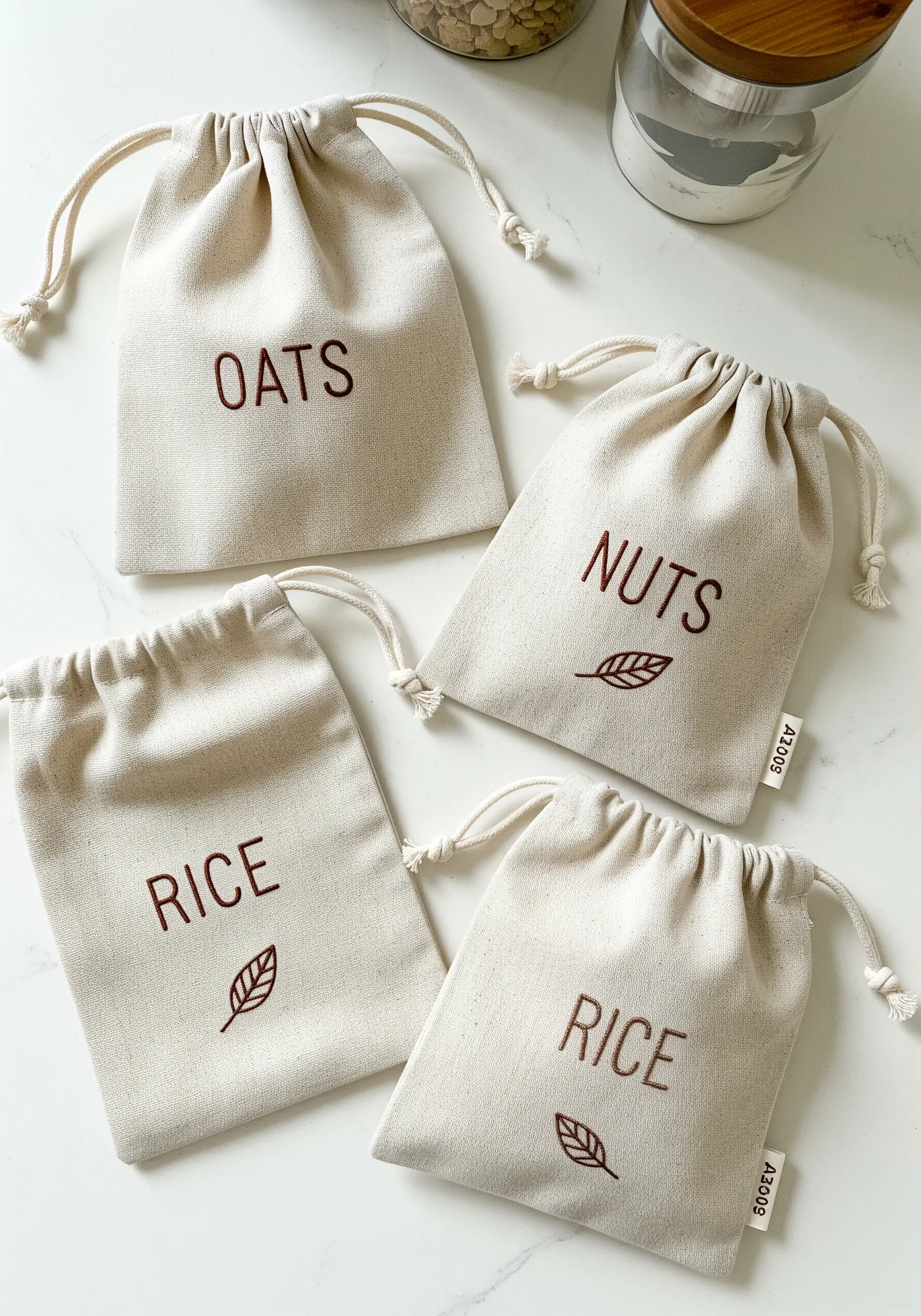 Canvas drawstring bags for pantry storage, embroidered with the words 'OATS', 'NUTS', and 'RICE'.
