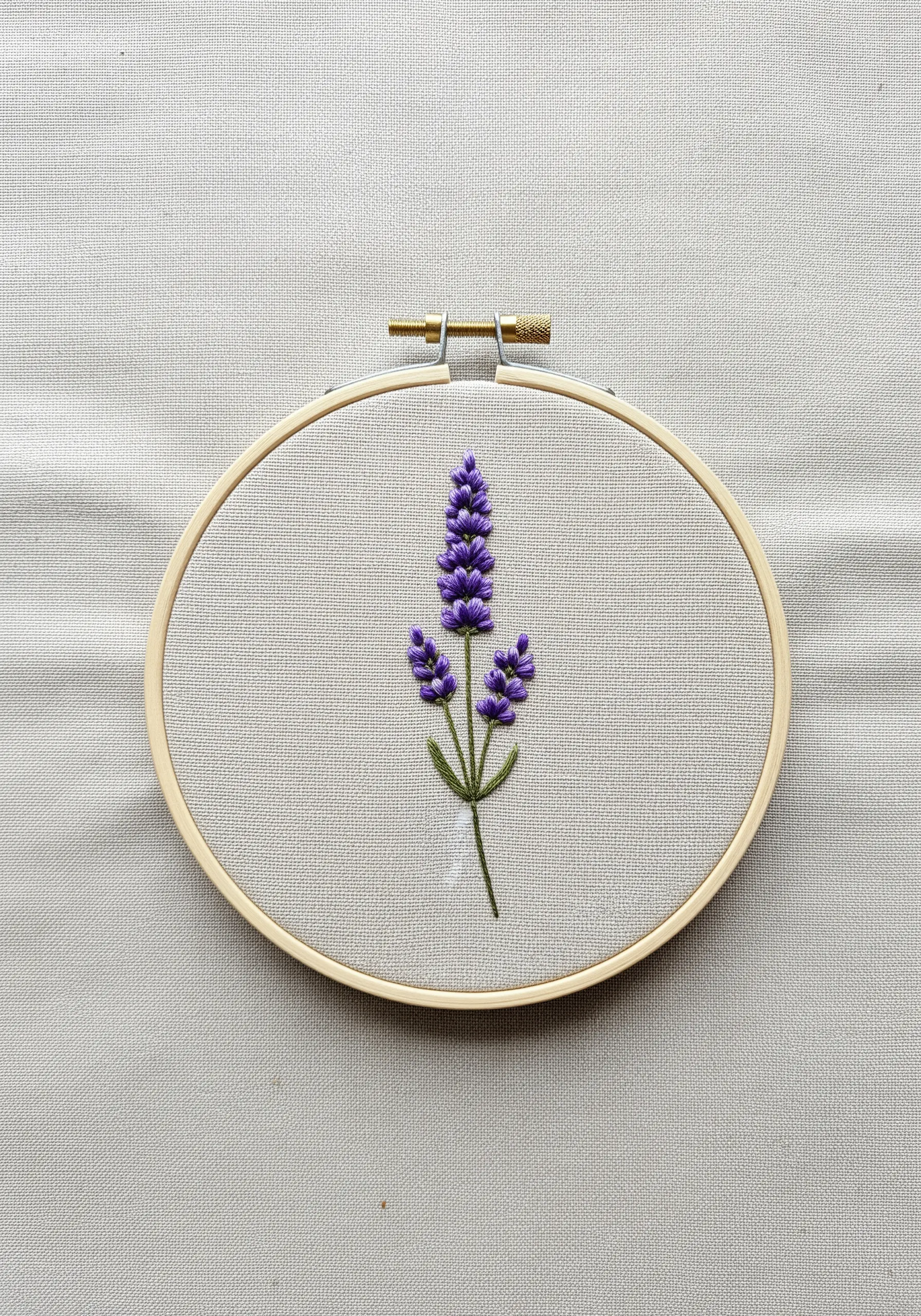 Hand-embroidered lavender sprig in a hoop with purple French knots and a green stem.