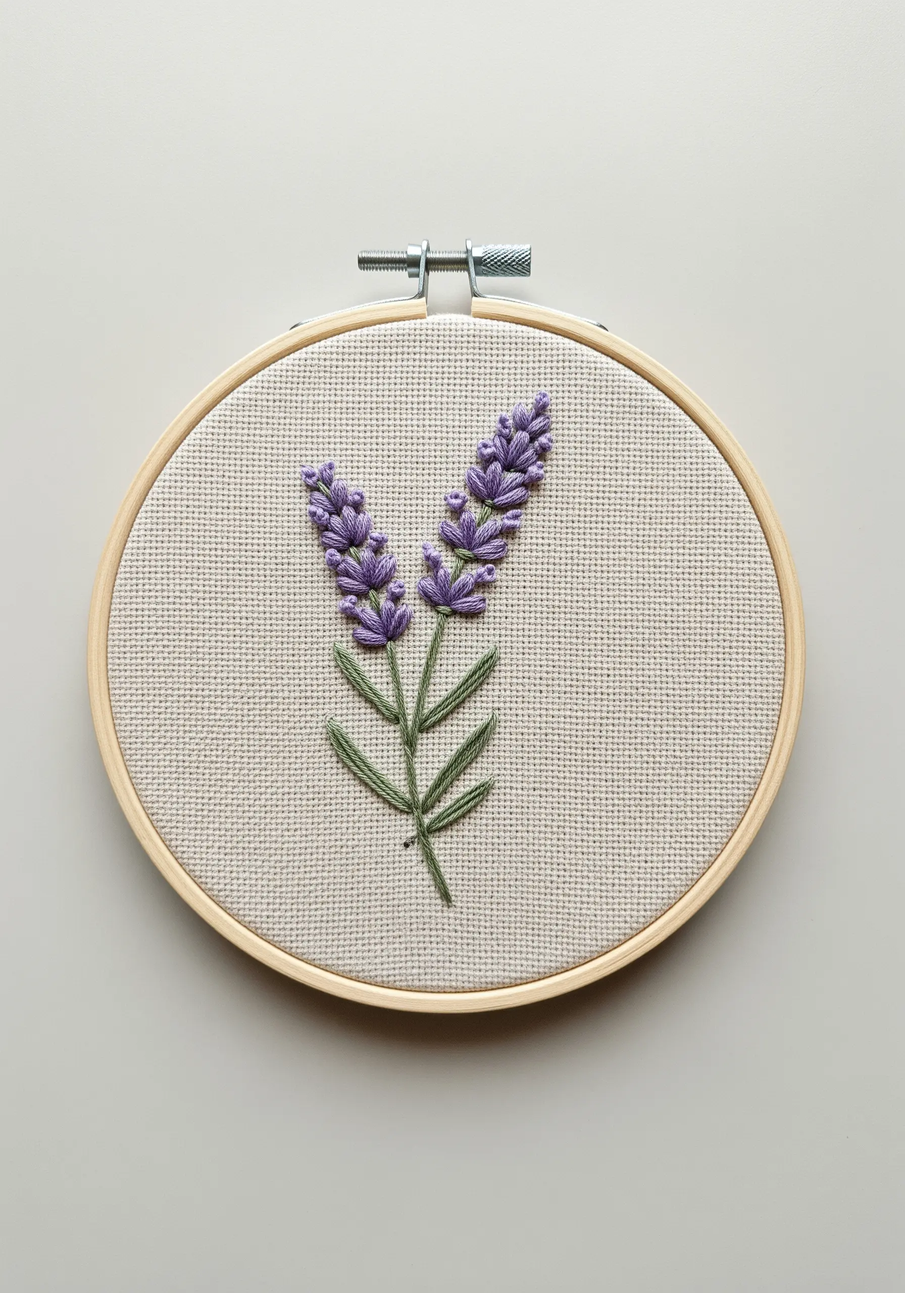 Two stalks of lavender embroidered with purple french knots and green stems in a hoop.