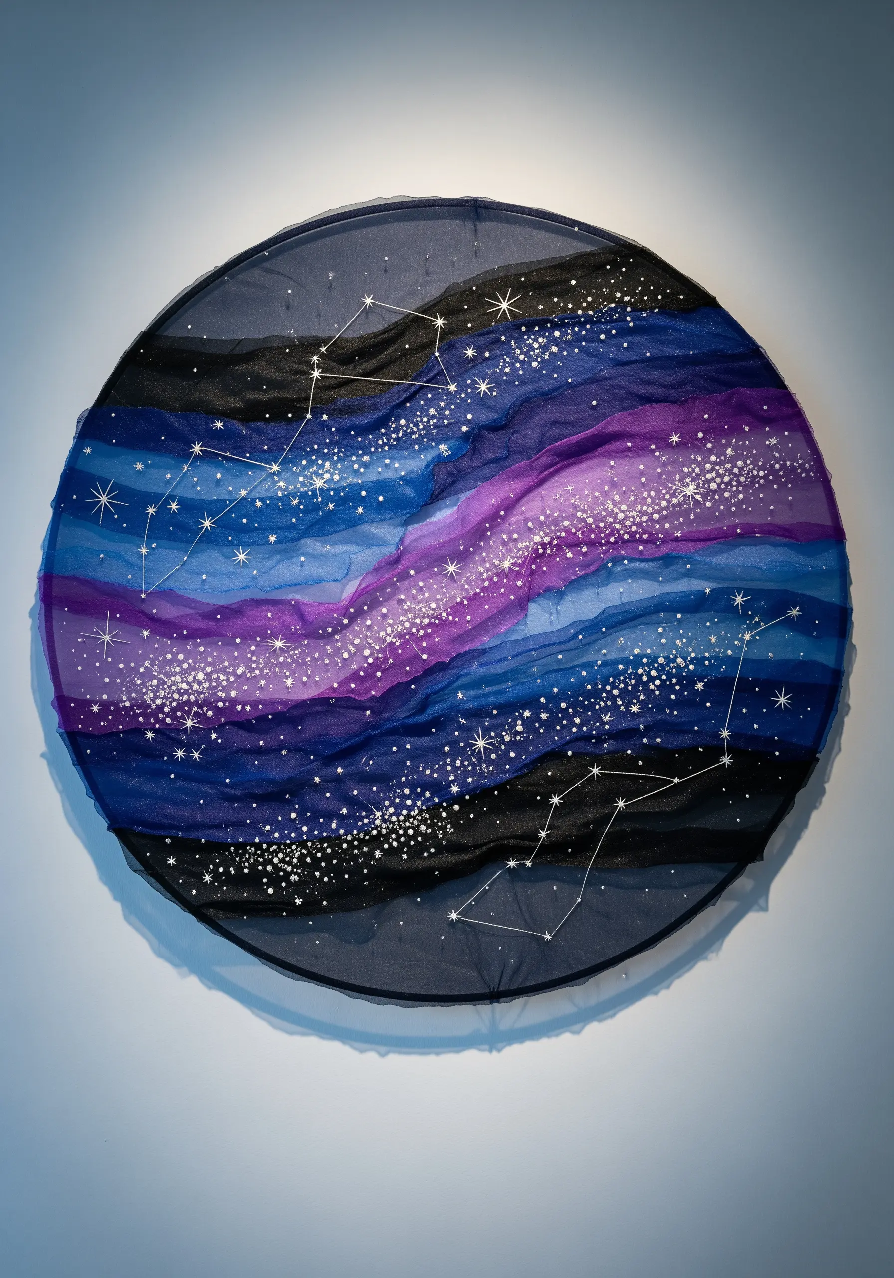 Circular hoop art with layered blue and purple sheer fabric creating a galaxy effect with star stitches.