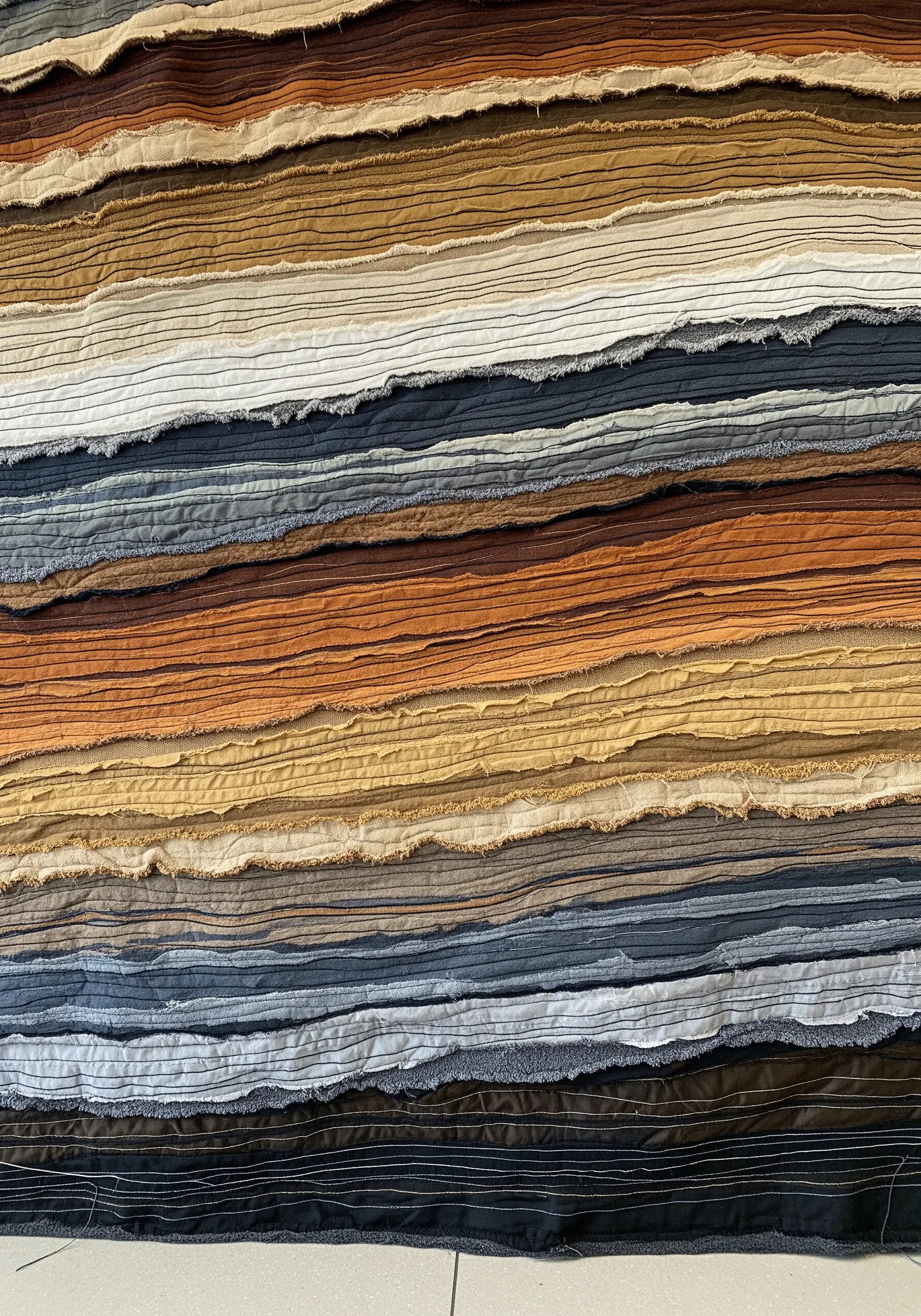 A close-up of a textile artwork with horizontal layers of raw-edged, earth-toned fabrics