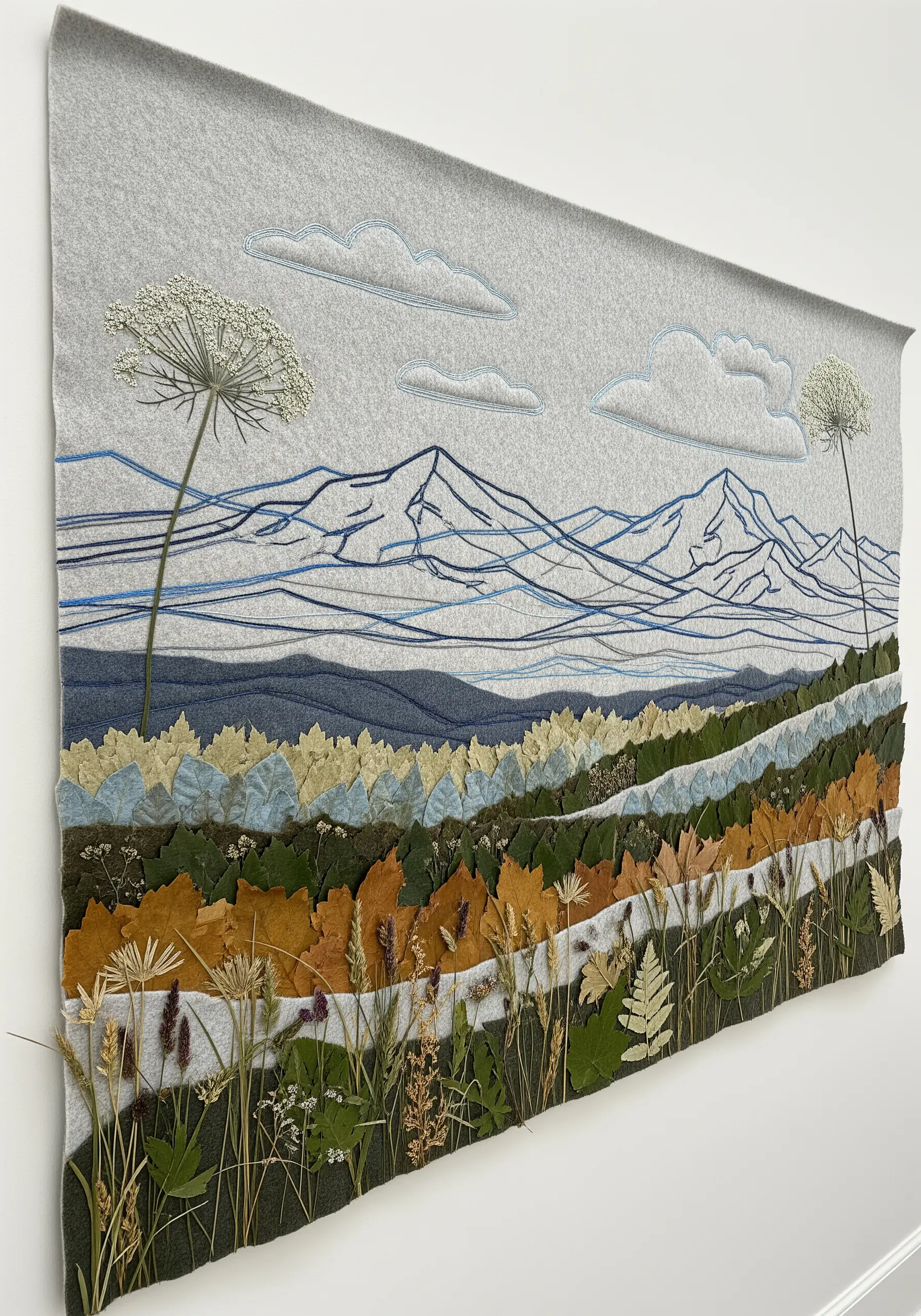 A mixed-media landscape with an embroidered mountain background, felt hills, and a foreground of pressed leaves.