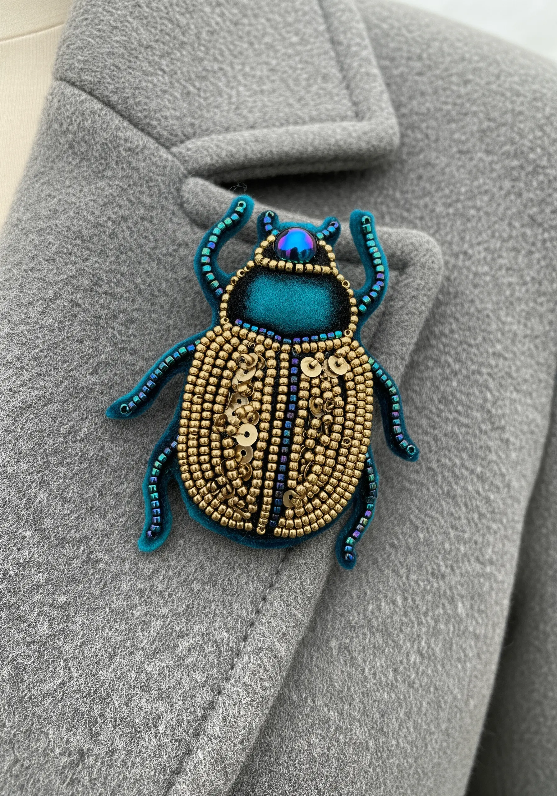 A jewel-toned beetle brooch made with beads, sequins, and felt on a coat lapel.