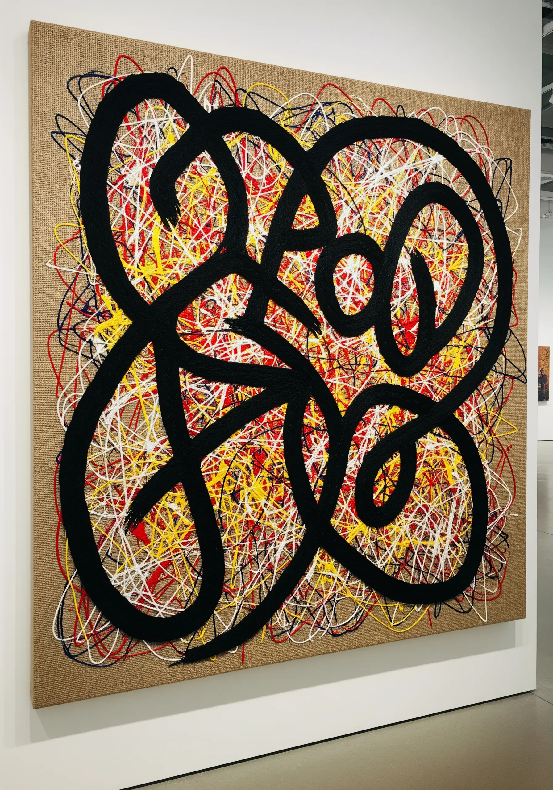 Large abstract canvas with a black motif over a colorful thread-splatter background.