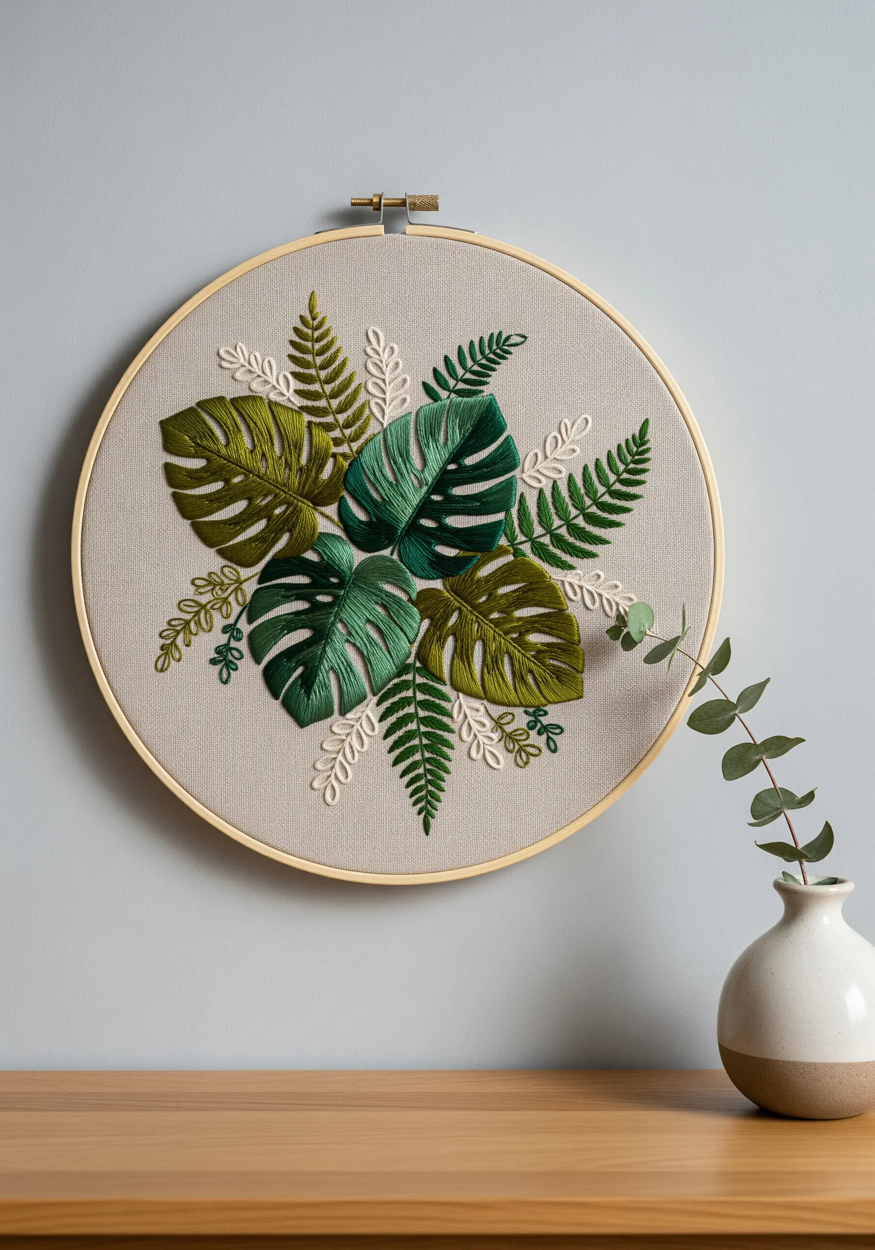 A botanical embroidery hoop with layered satin stitch monstera leaves and ferns.