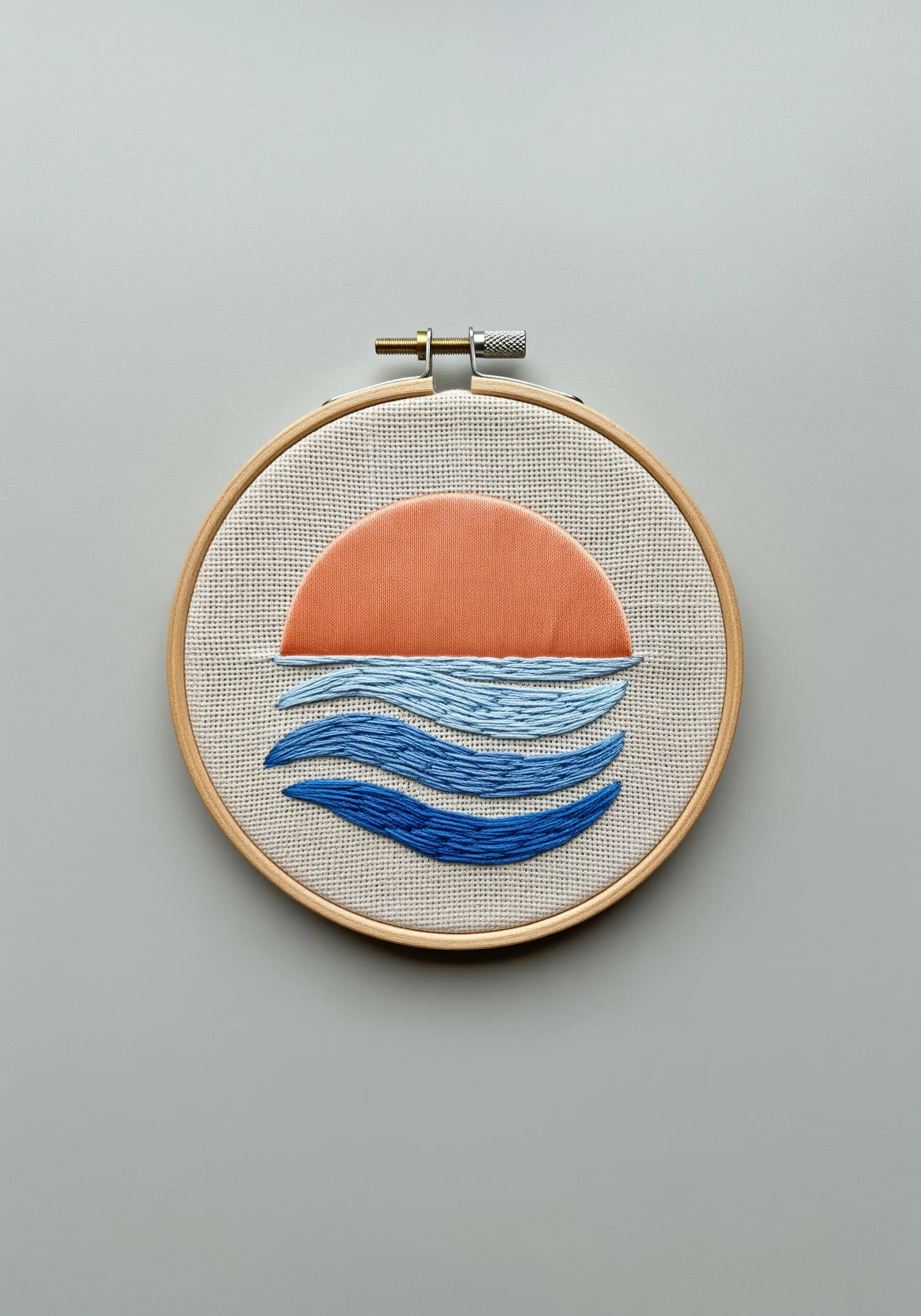 An embroidered sunset over water, with layered blue satin stitches for the waves.
