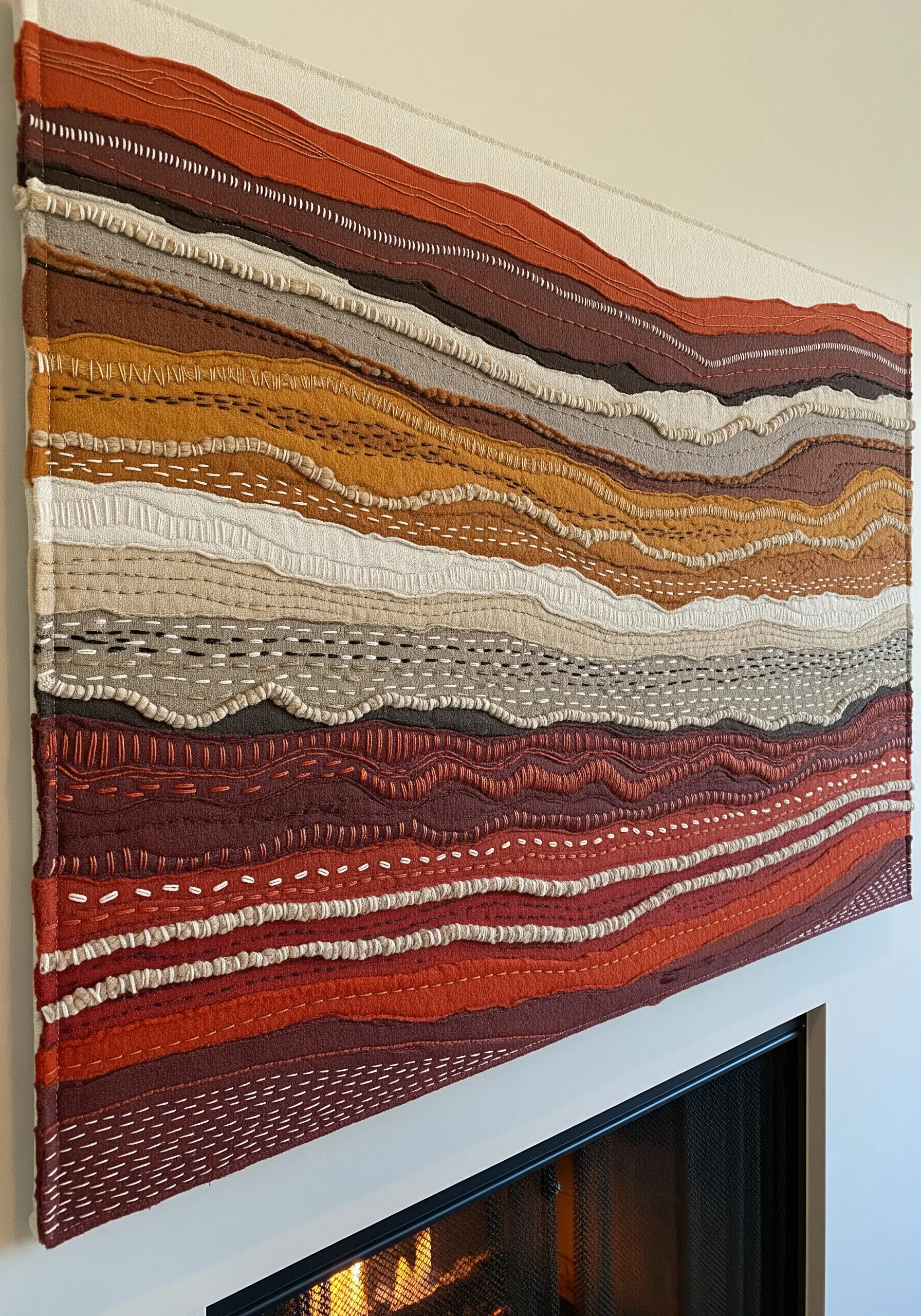 A large textile wall art piece with layered, earthy-toned fabrics and decorative running stitches.