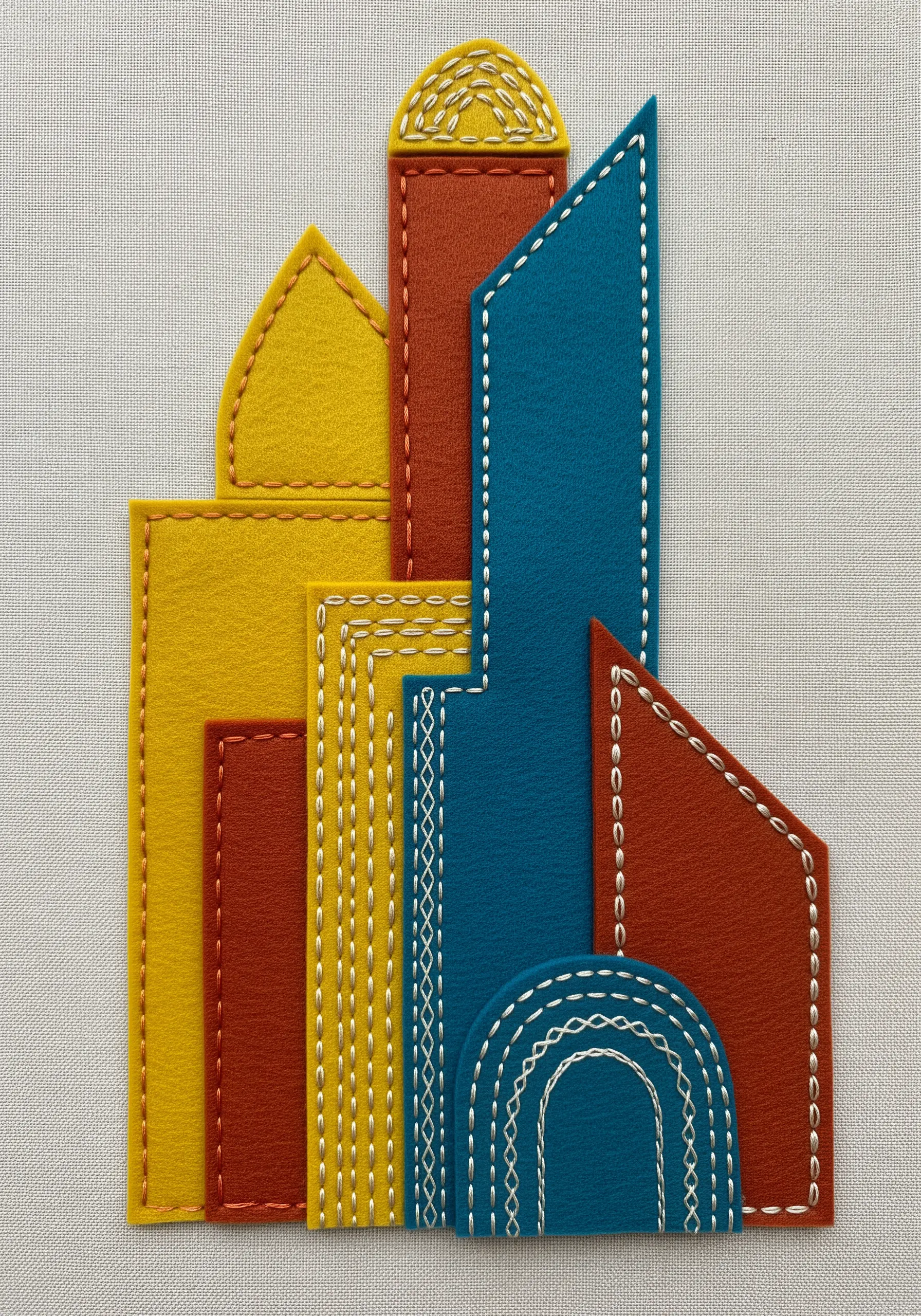 Geometric felt shapes in yellow, red, and blue layered and outlined with decorative white stitches