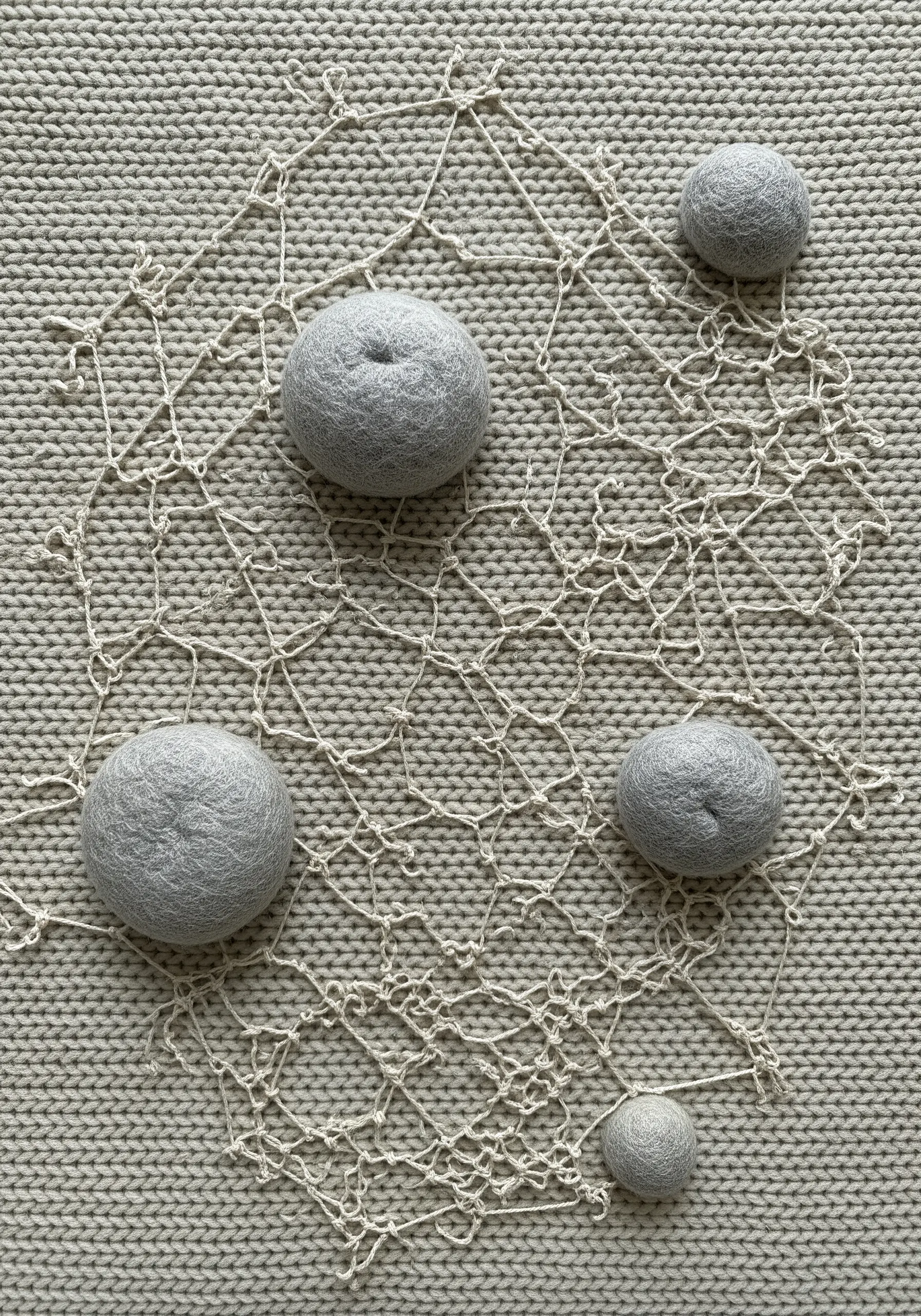 Grey felted wool balls attached to a delicate thread web on a grey knit fabric background.
