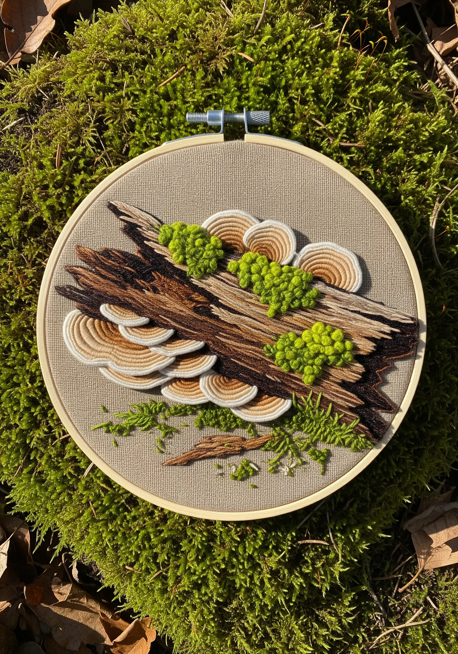 Turkey tail mushrooms and moss embroidered on a log, showcasing layered satin stitch.