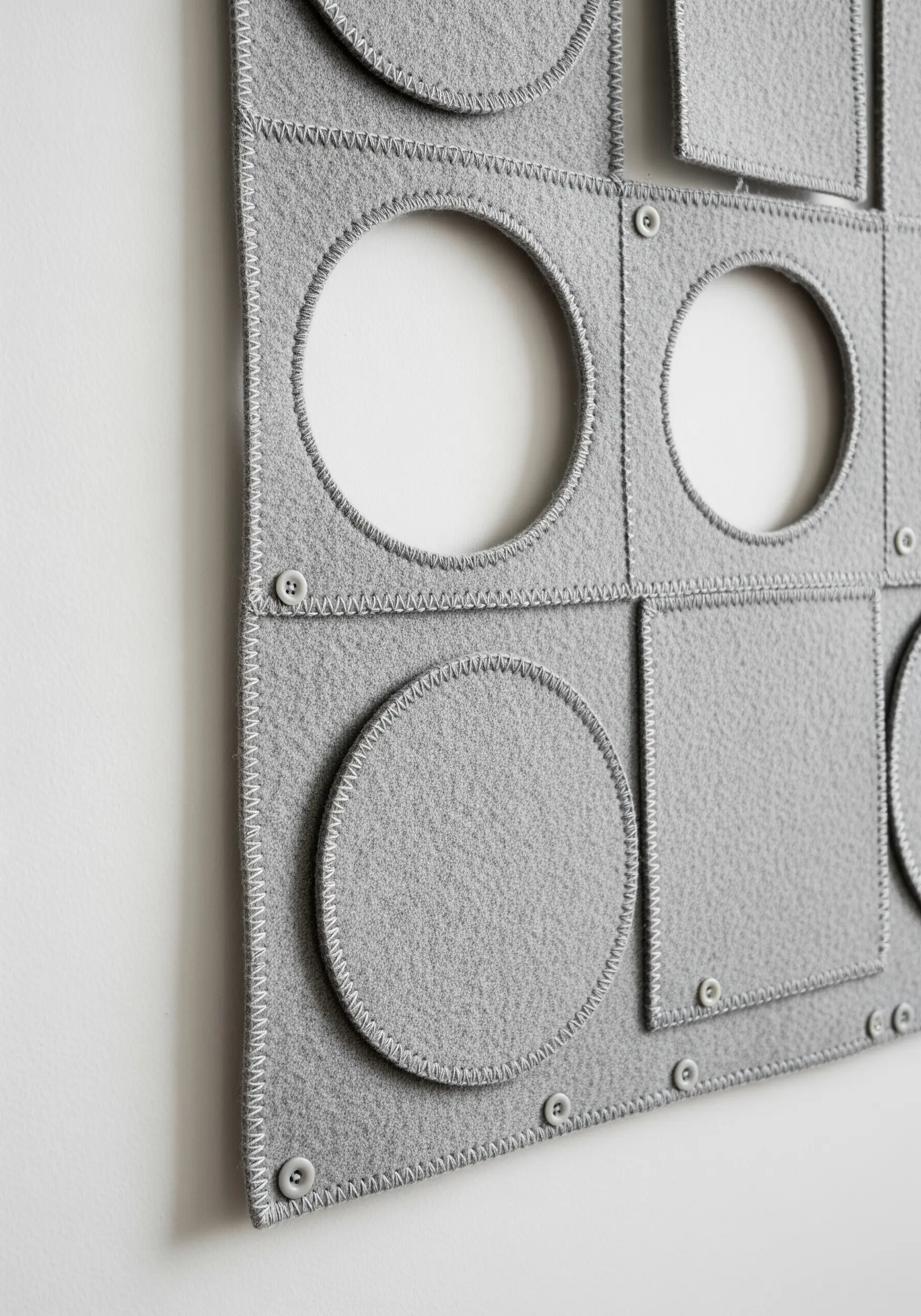 A close-up of layered gray felt panels with cut-out shapes and visible zigzag stitching.