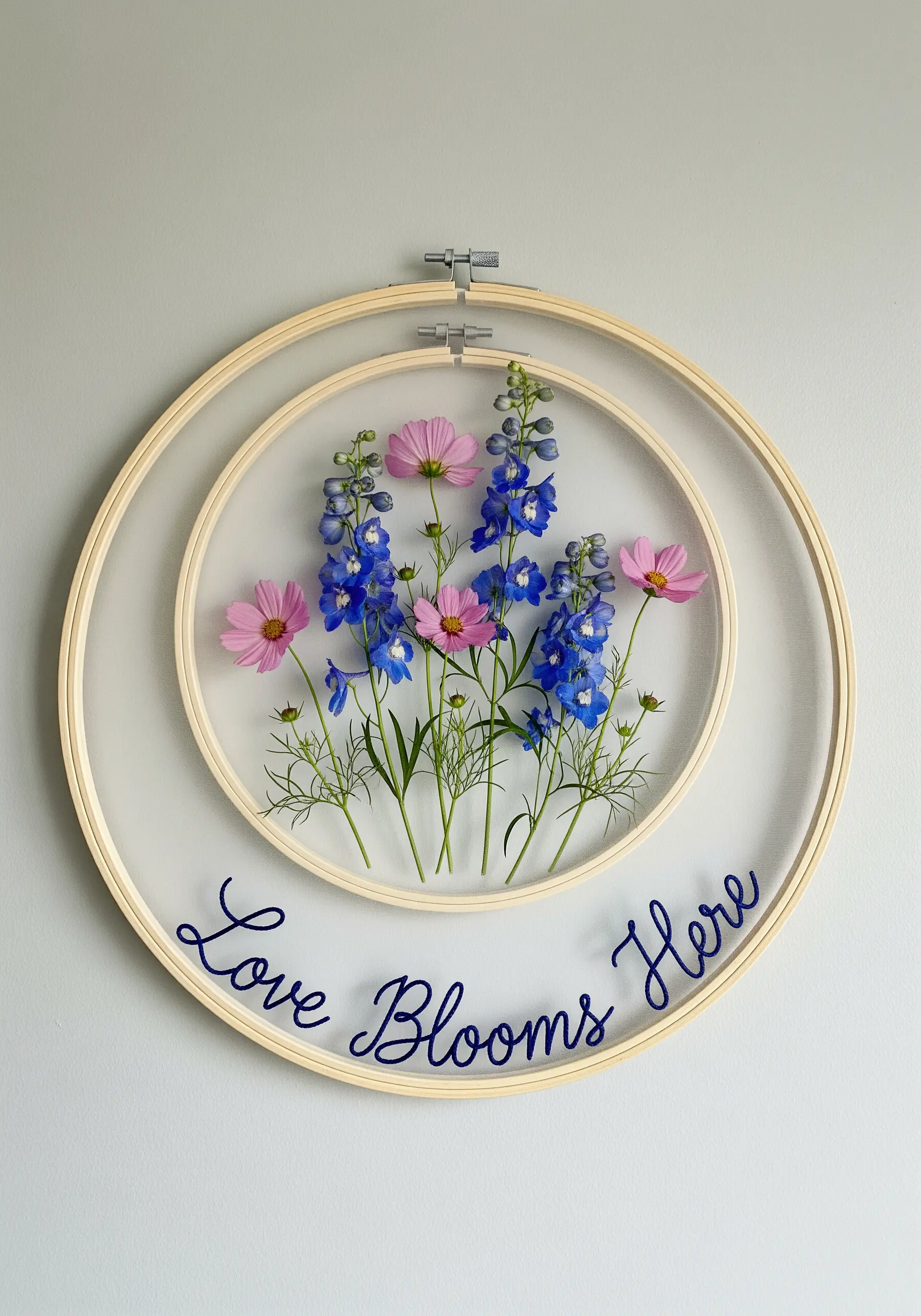 Layered embroidery hoops with pressed flowers on a sheer background and an embroidered quote.