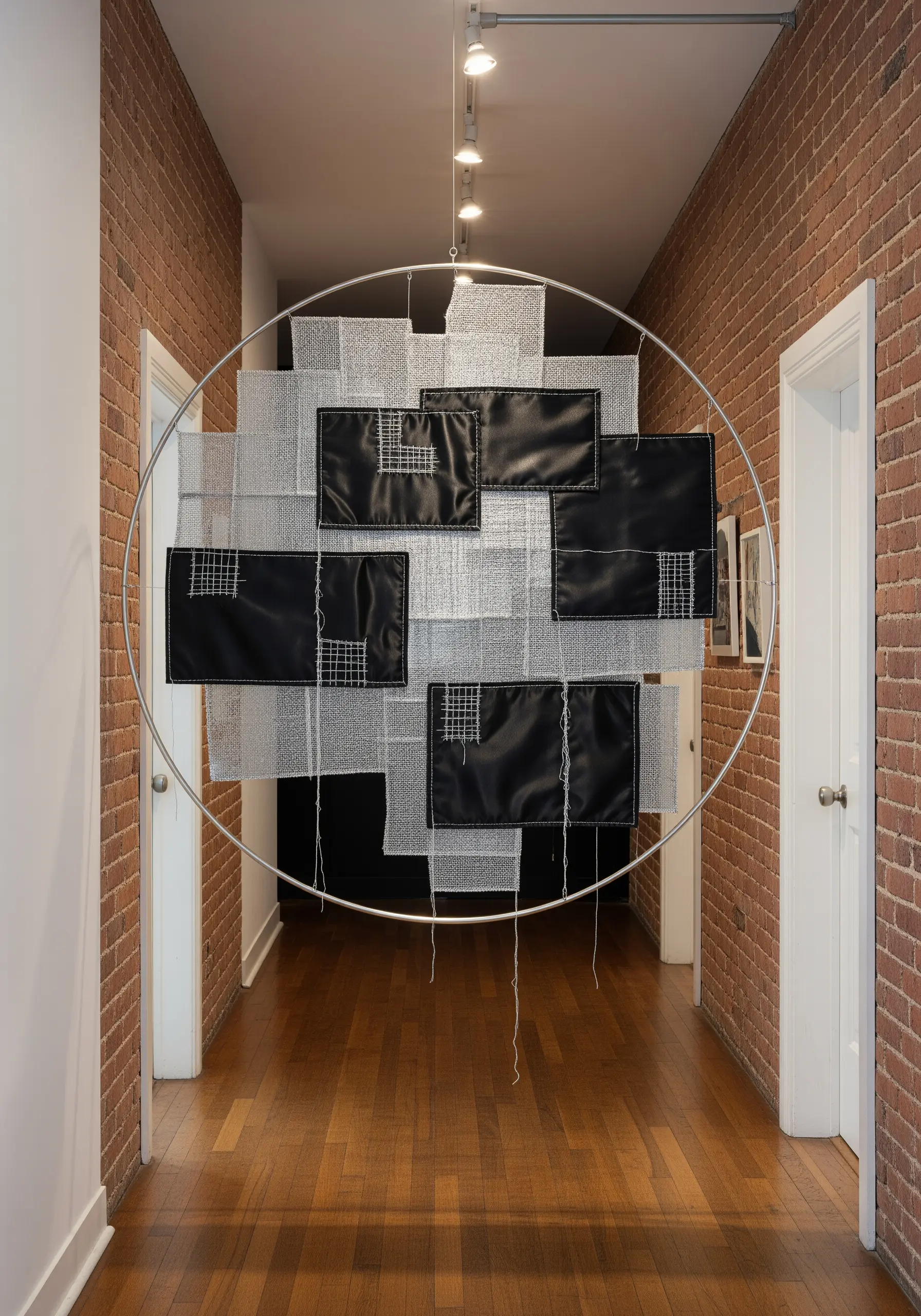 A large mixed-media embroidery installation using silver mesh, black fabric panels, and white thread.