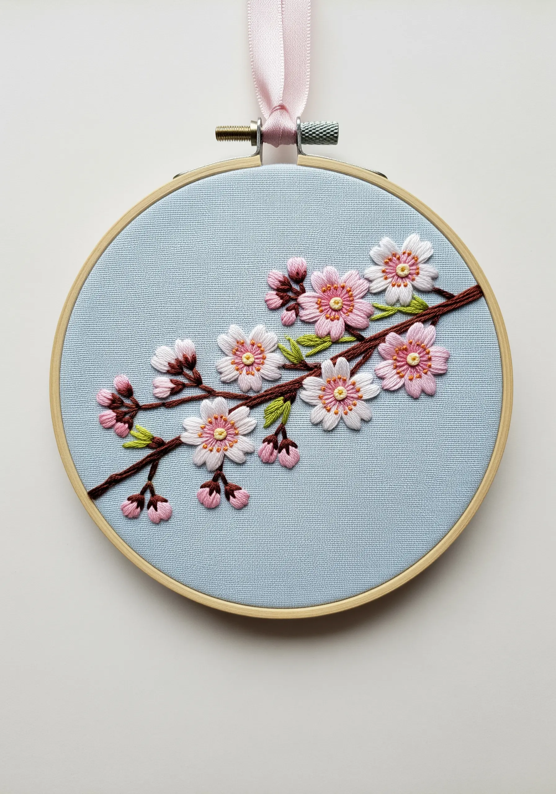 A branch of cherry blossoms embroidered on blue fabric, with pink and white flowers