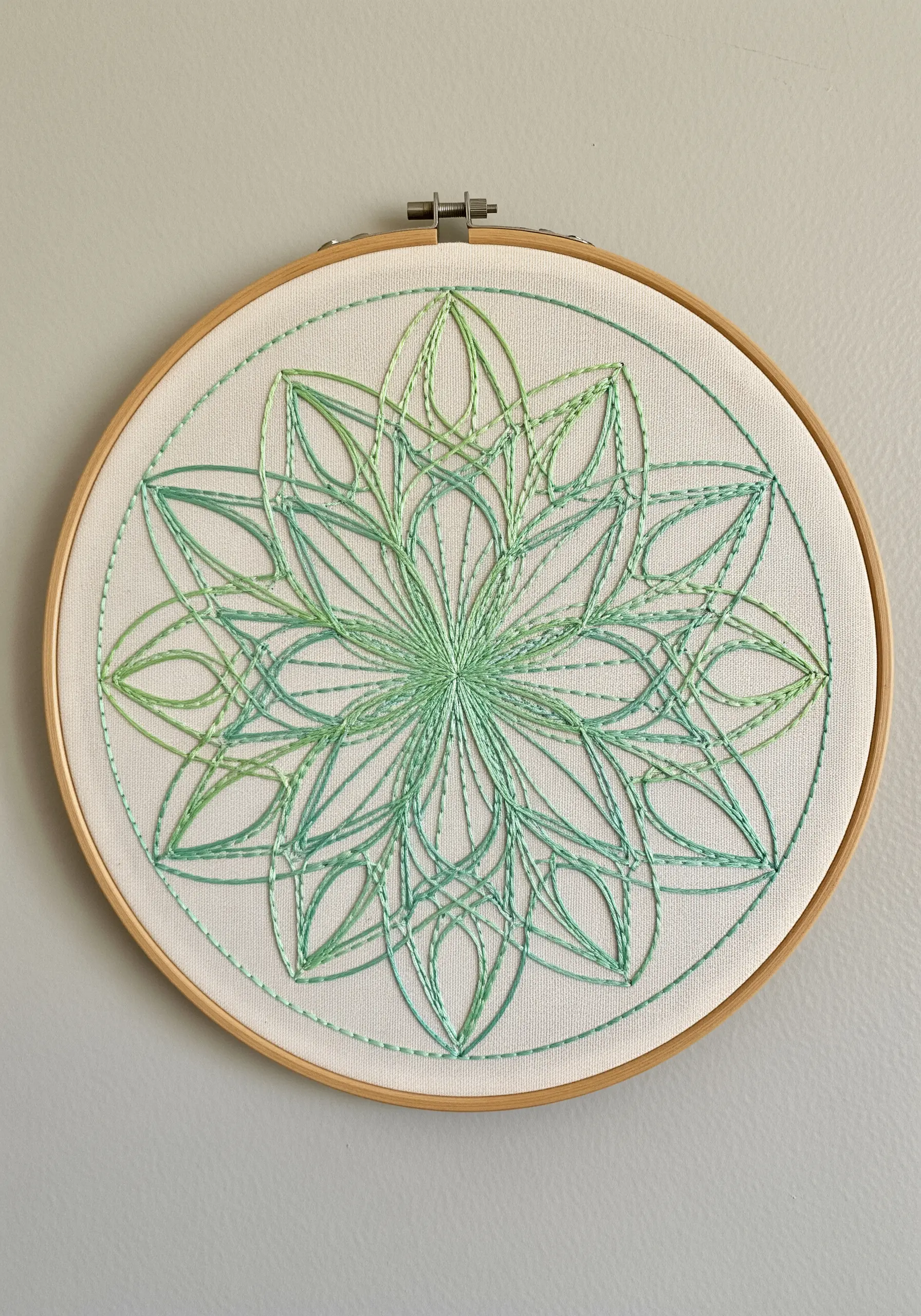 A geometric floral mandala stitched with overlapping lines of green gradient threads.