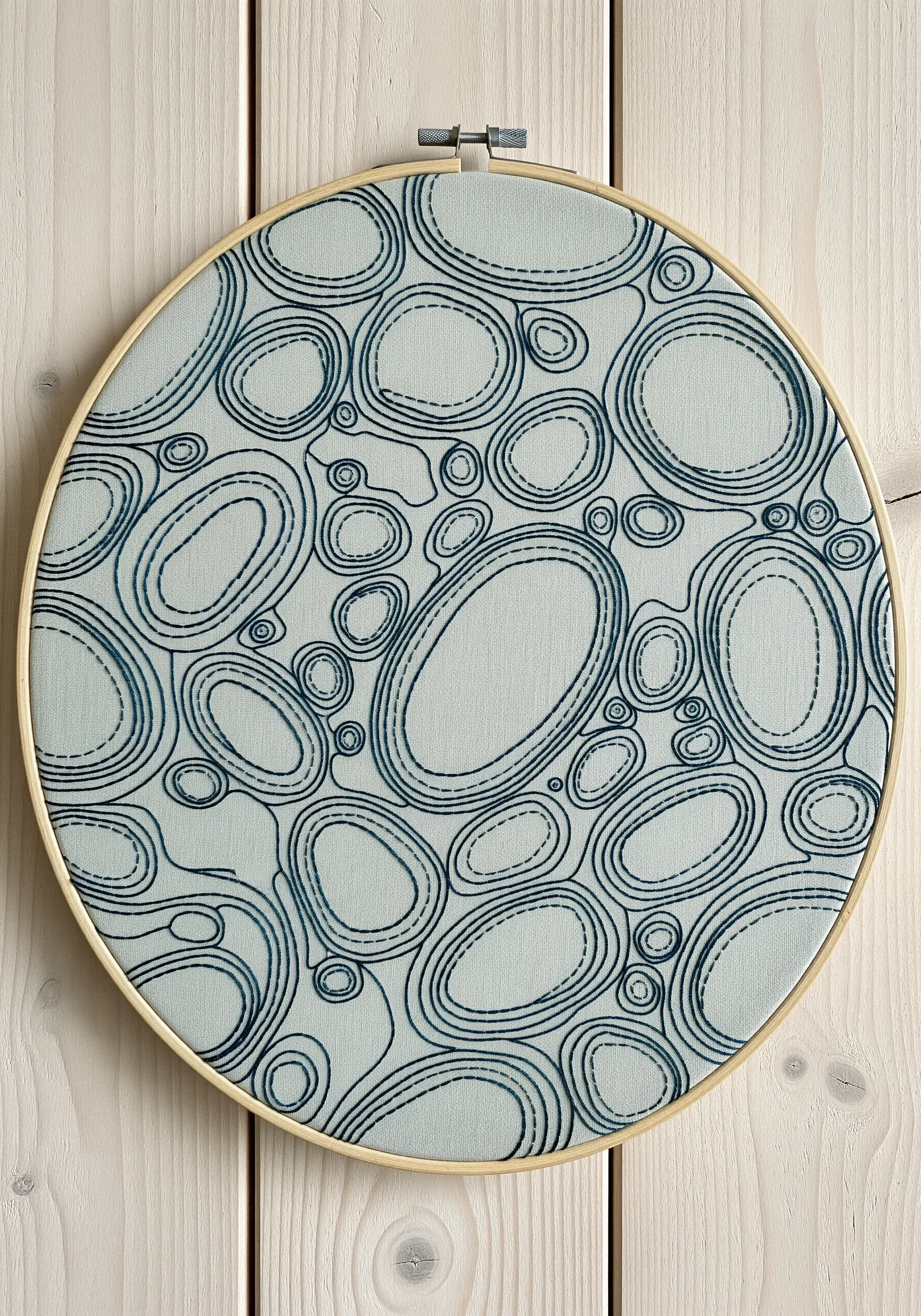Abstract overlapping oval shapes outlined in layered, sketch-like stitches on pale blue fabric.