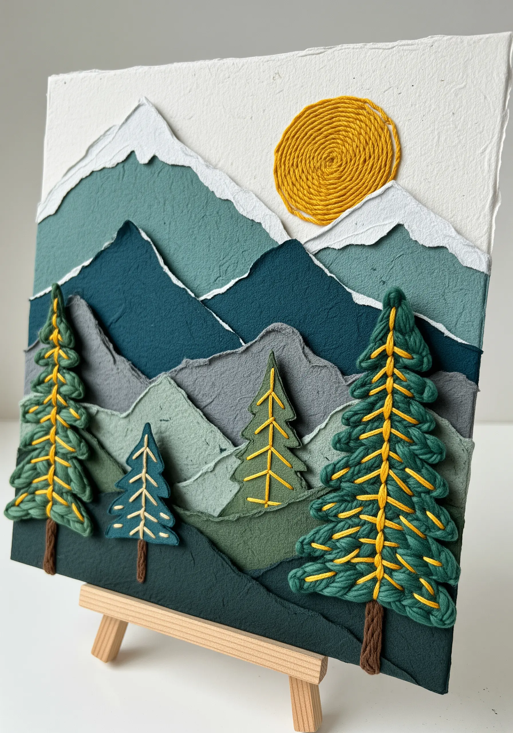 Layered paper mountain scene with embroidered trees and a coiled yarn sun.