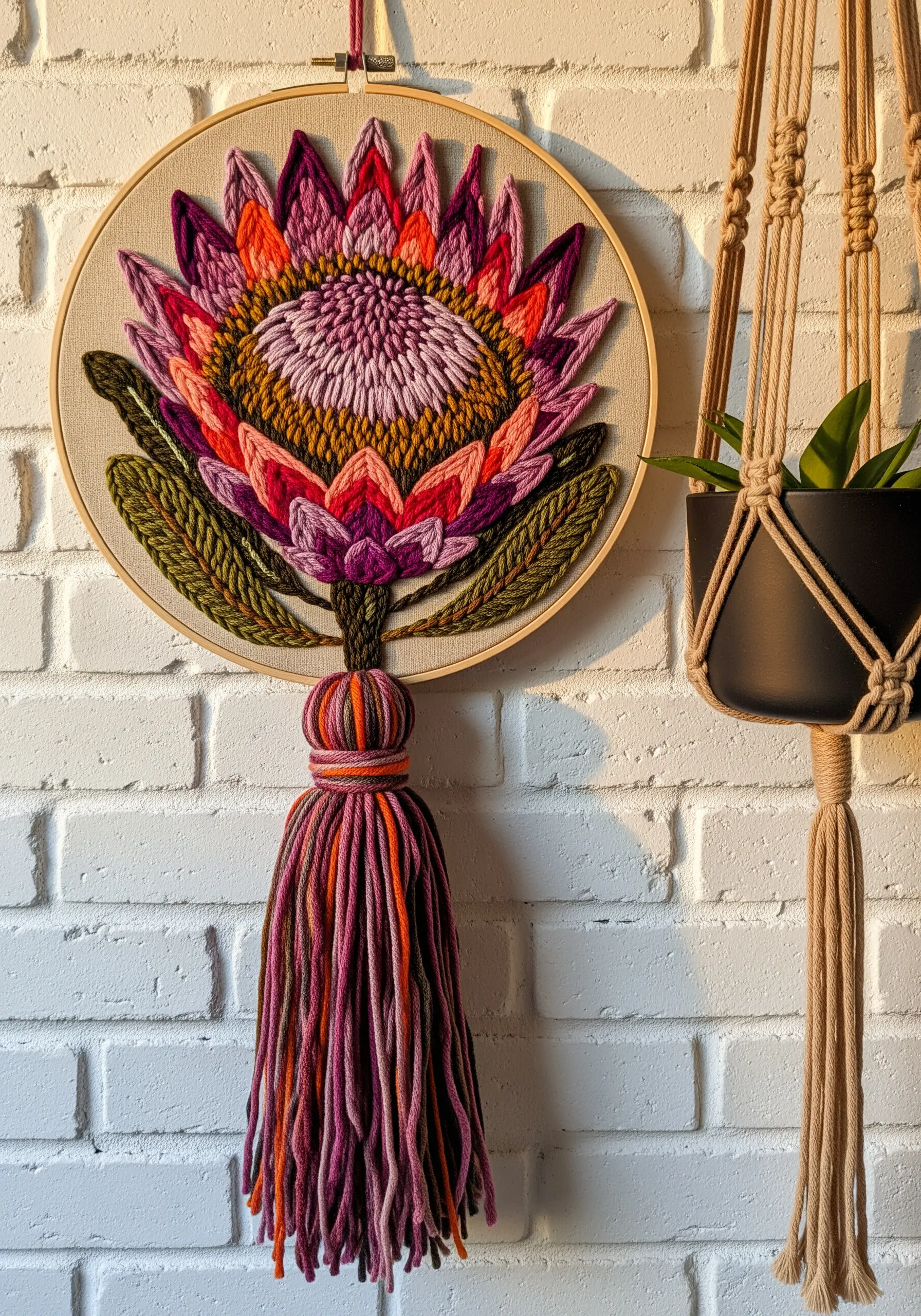 Embroidered protea flower in a hoop with a large, multicolored yarn tassel hanging below.
