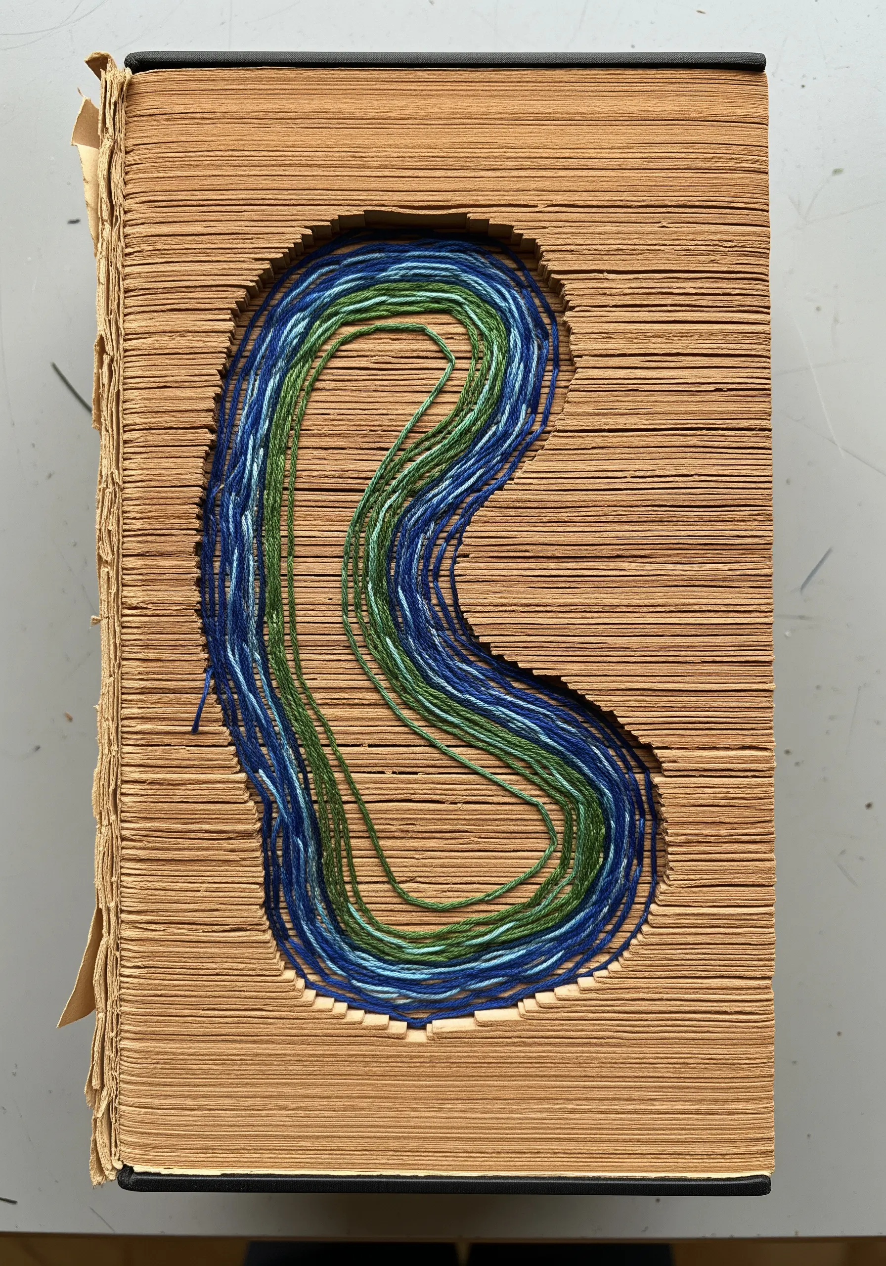 An old book with a hollowed-out center filled with layers of blue and green thread.