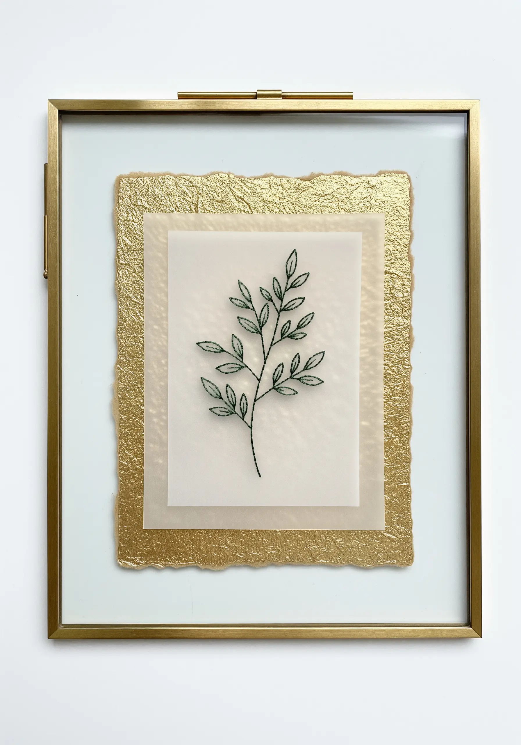A simple green branch embroidered on vellum, layered over gold paper in a floating frame.