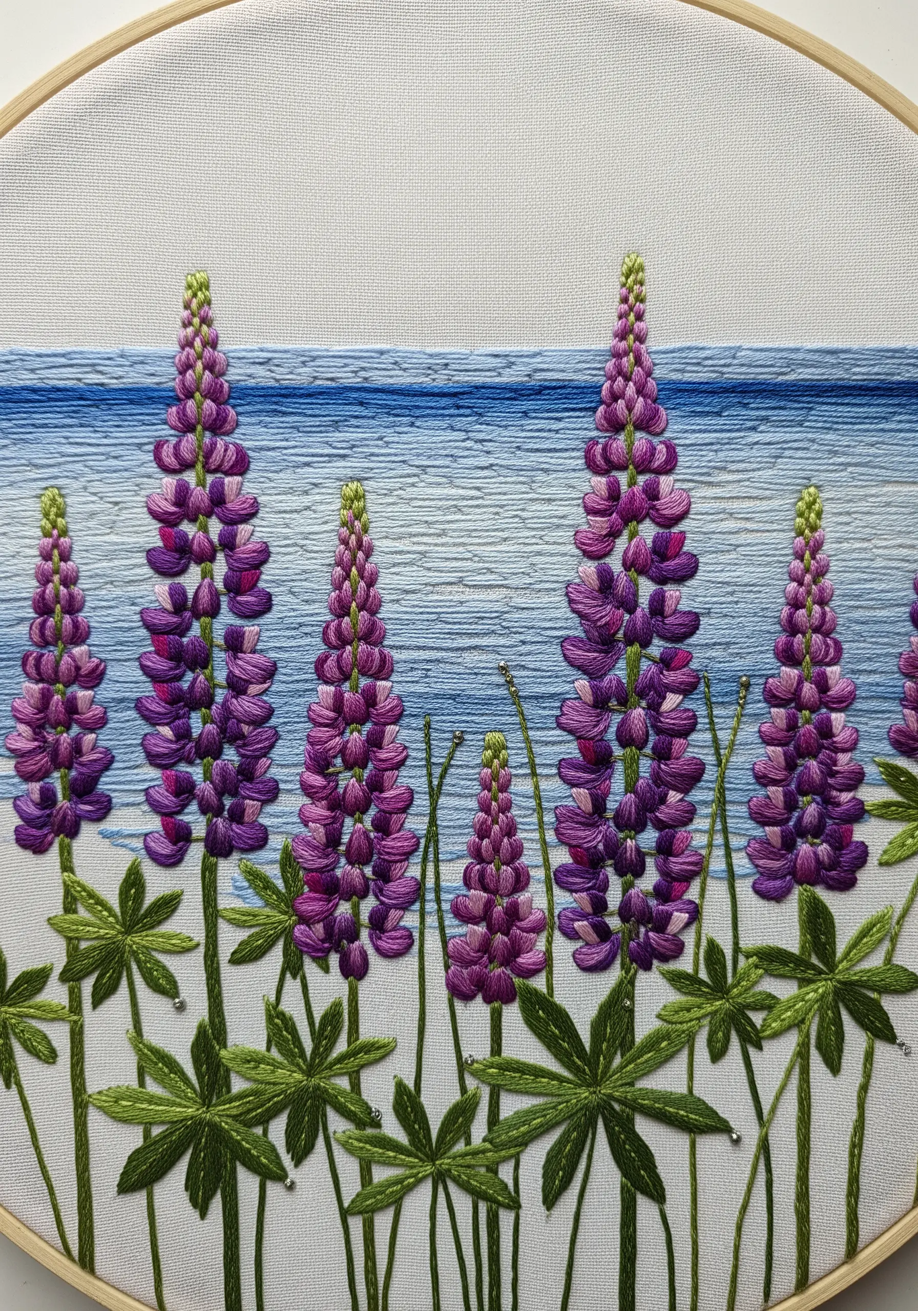 Purple lupine flowers embroidered in the foreground of a calm, blue satin-stitched lake.