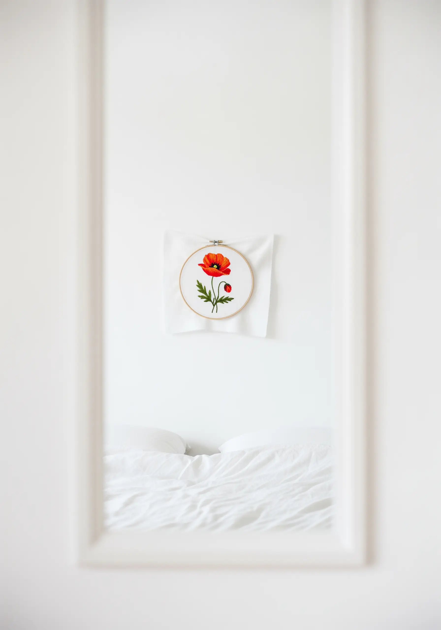 A single, vibrant red poppy embroidered in a hoop, seen through a doorway.