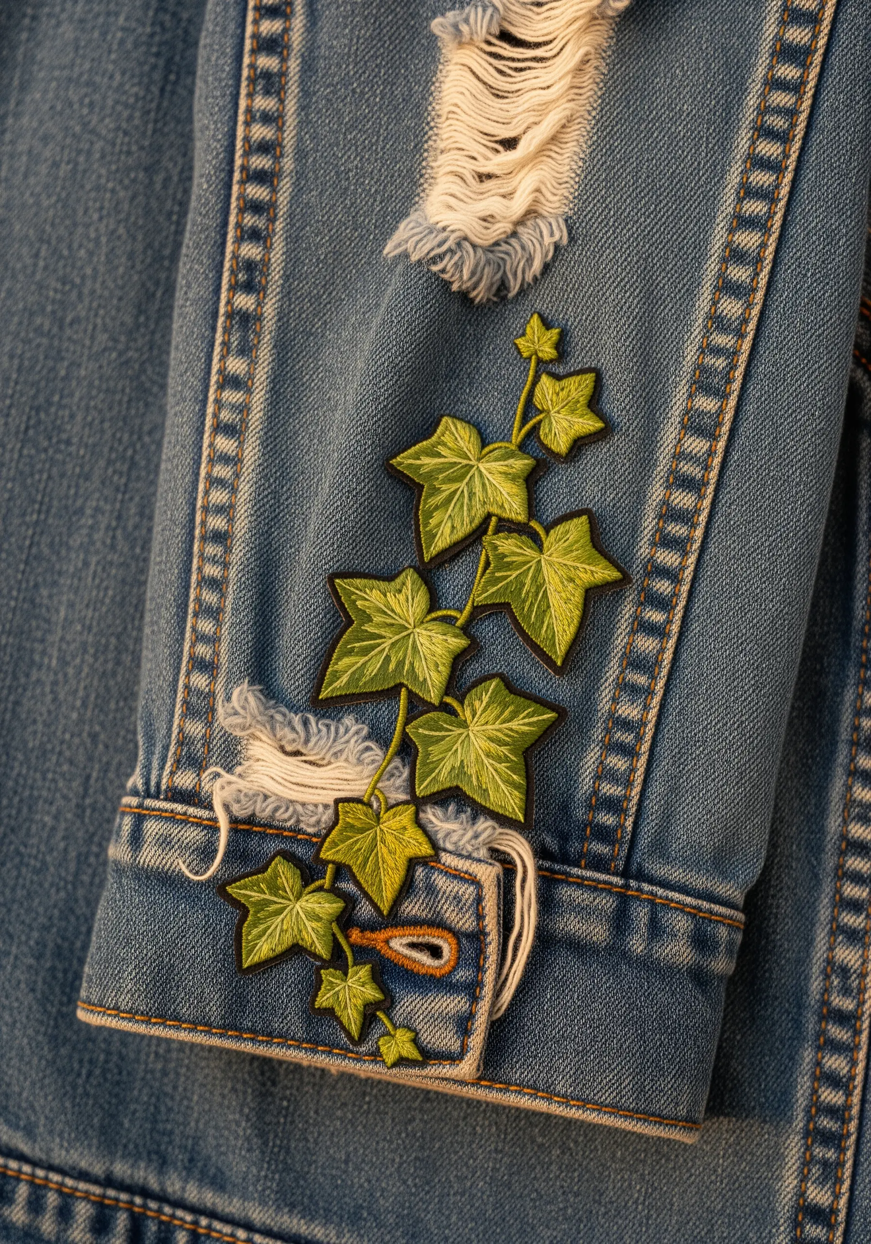 Embroidered ivy vine patch climbing up the cuff and sleeve of a distressed denim jacket.