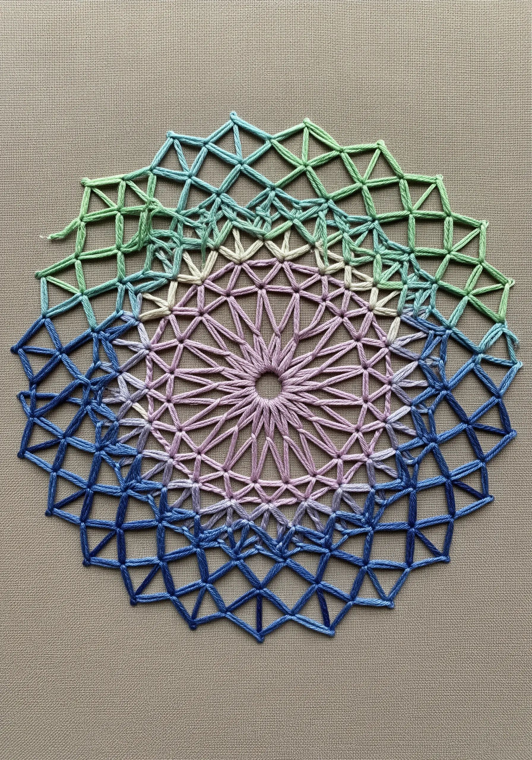 A geometric lace-like mandala stitched with variegated thread in a rainbow gradient.