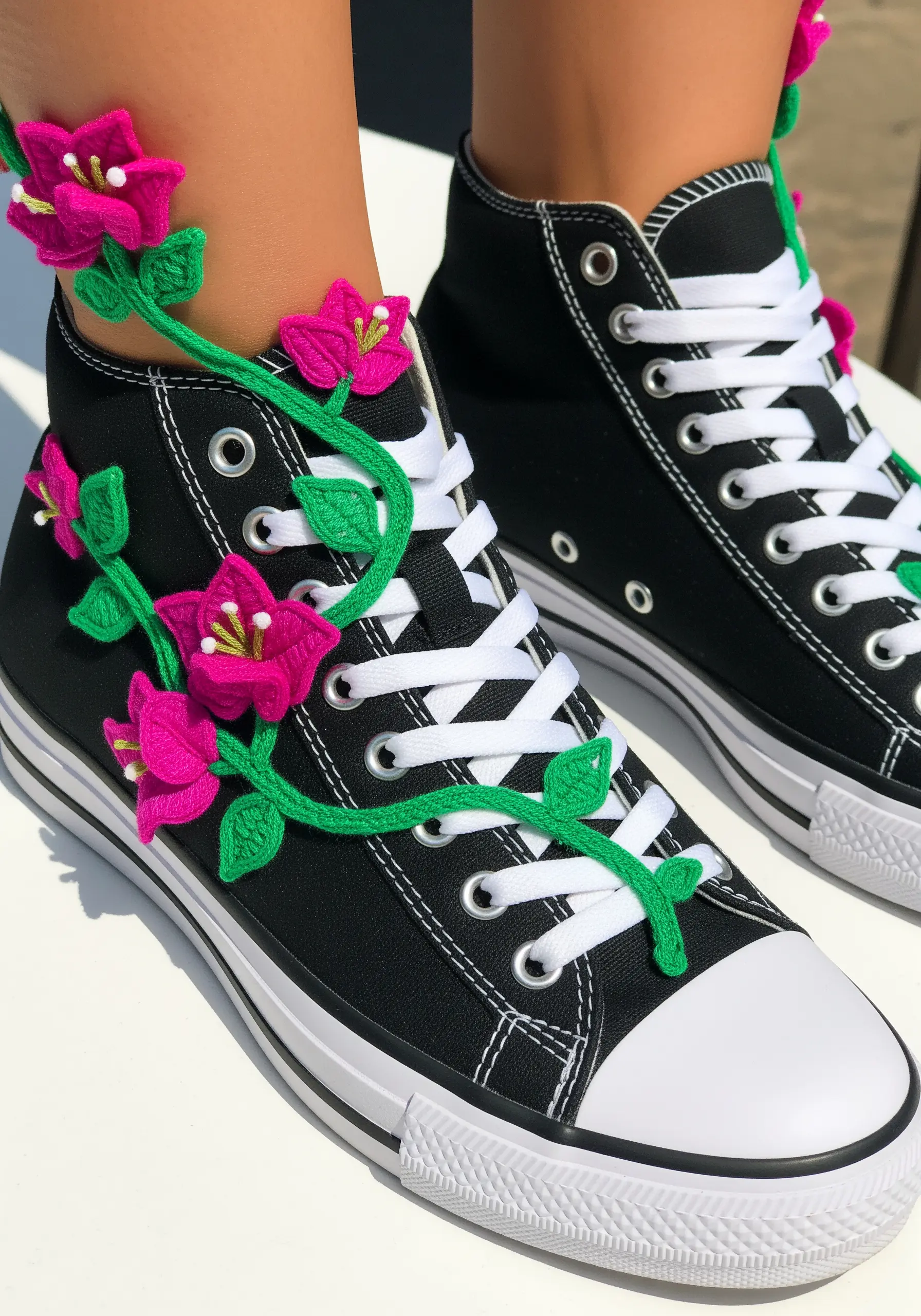 A 3D vine with pink flowers woven through the laces of a black high-top sneaker.