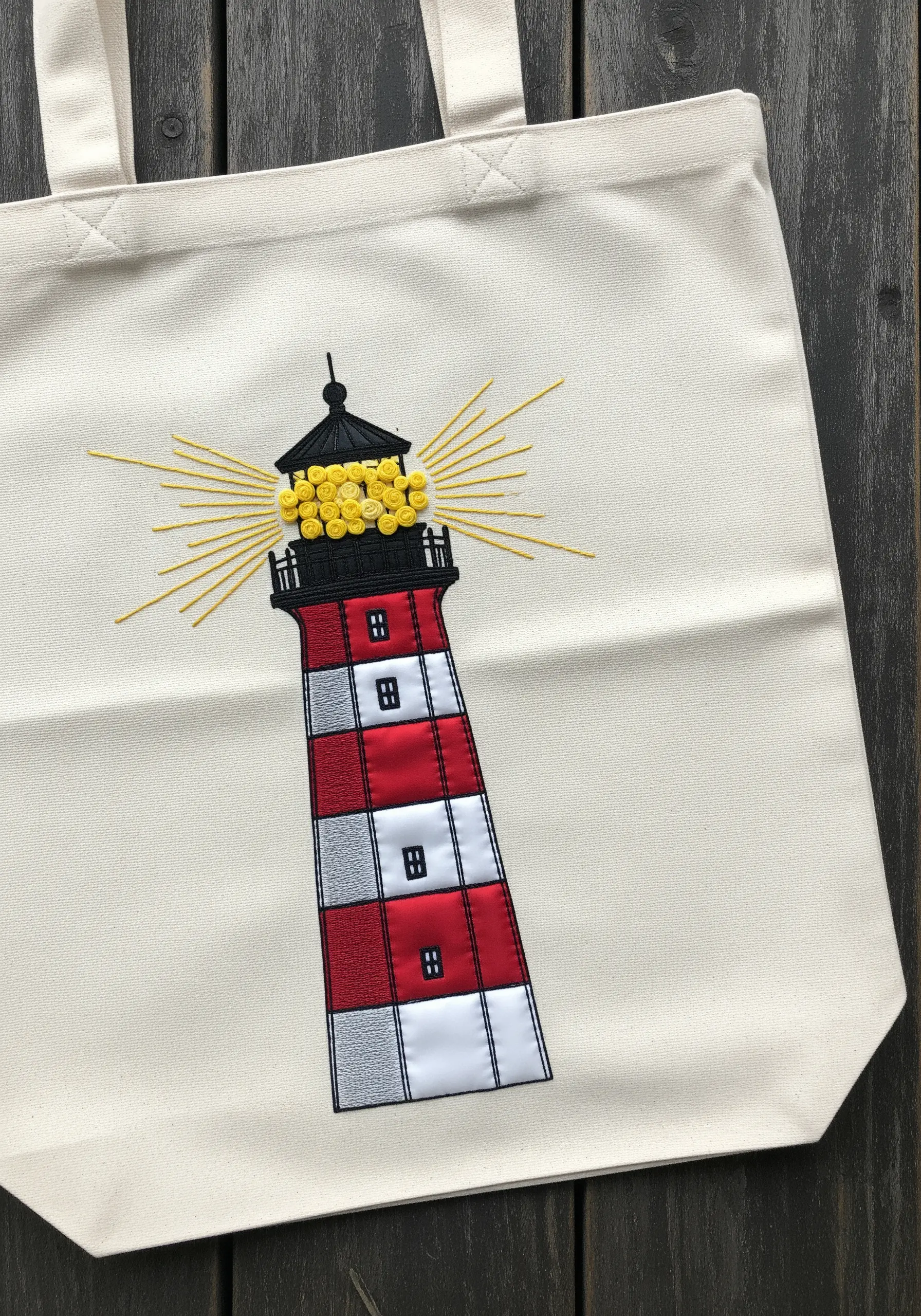 An embroidered and appliquéd lighthouse with 3D French knot light on a canvas tote.