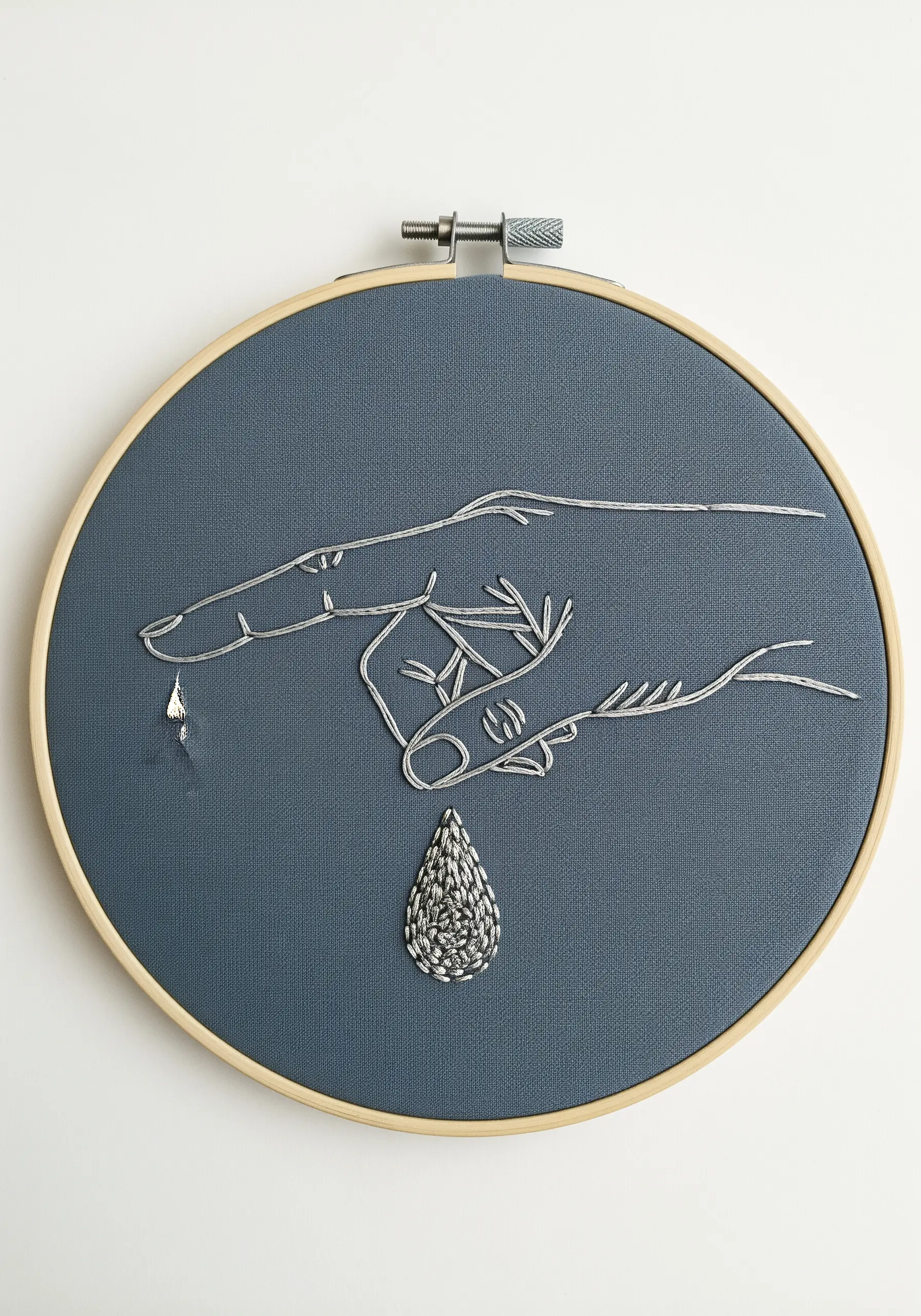 A hand stitched in silver metallic thread, with a single, shimmering embroidered teardrop.