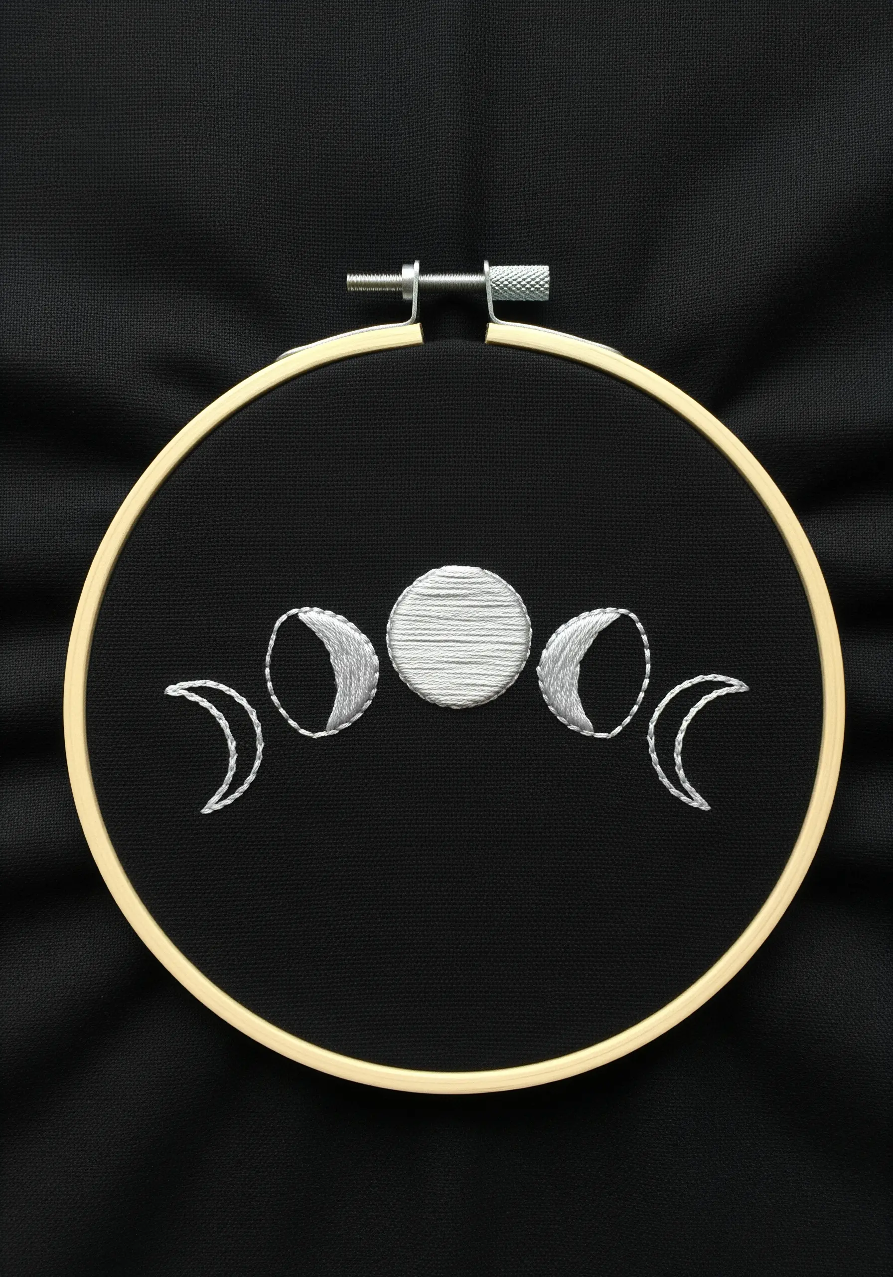 Embroidered moon phases in silver and grey thread on black fabric.