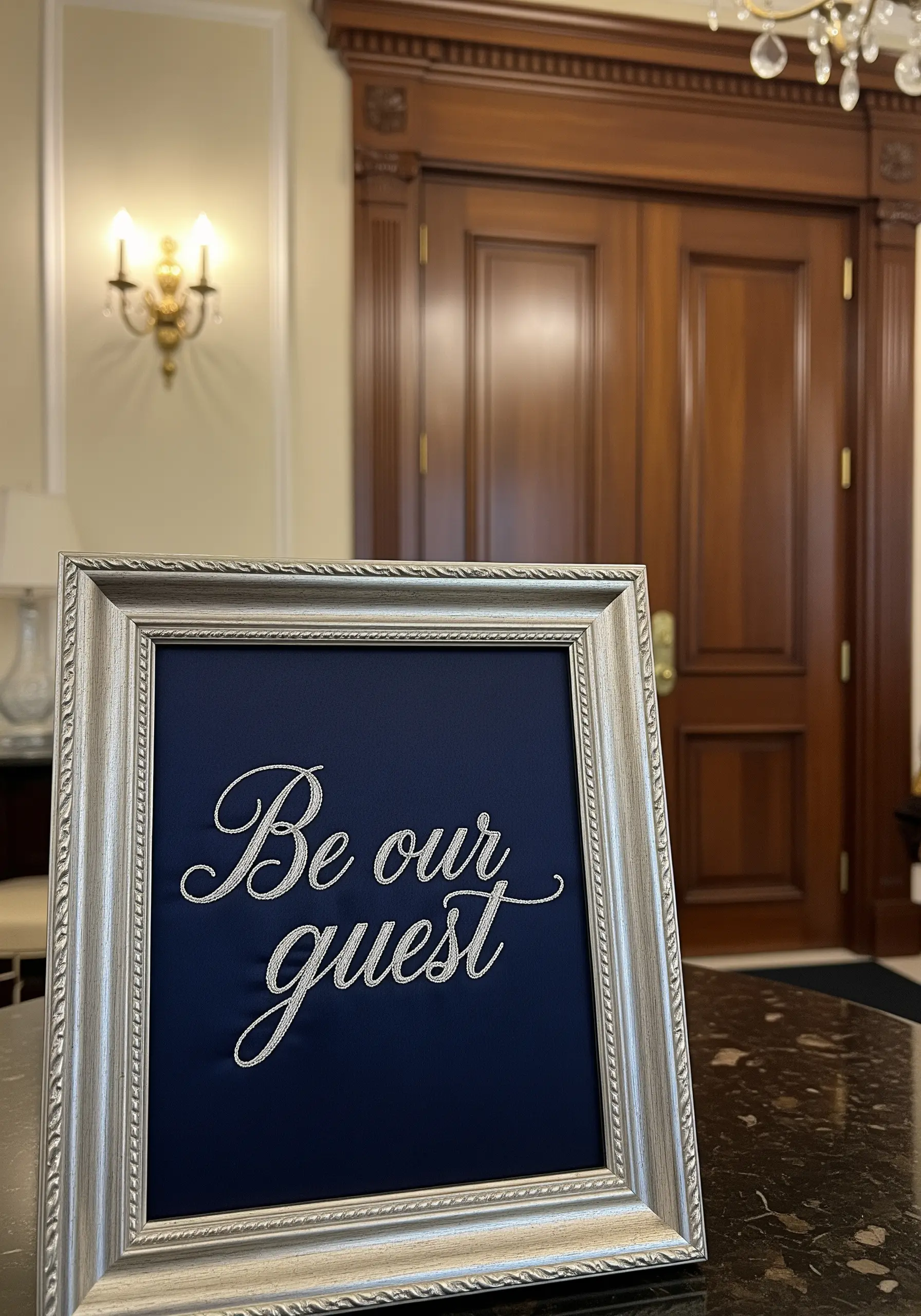 'Be our guest' embroidered in elegant silver metallic thread on a navy blue background.