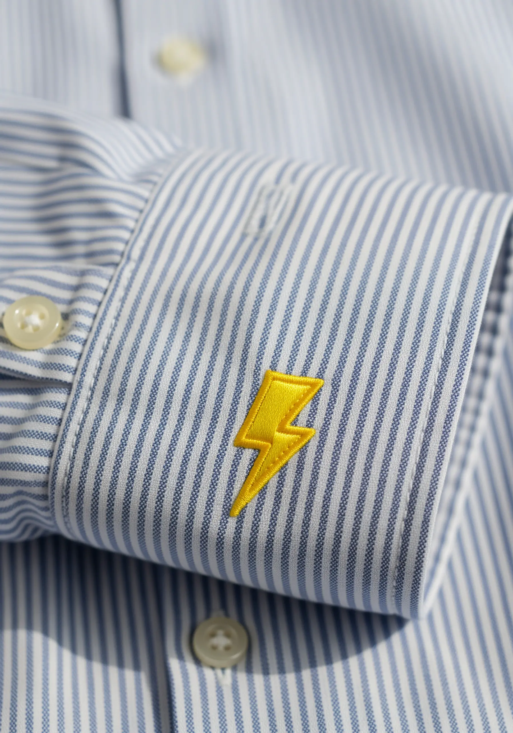 Bright yellow lightning bolt embroidered on the cuff of a striped shirt.