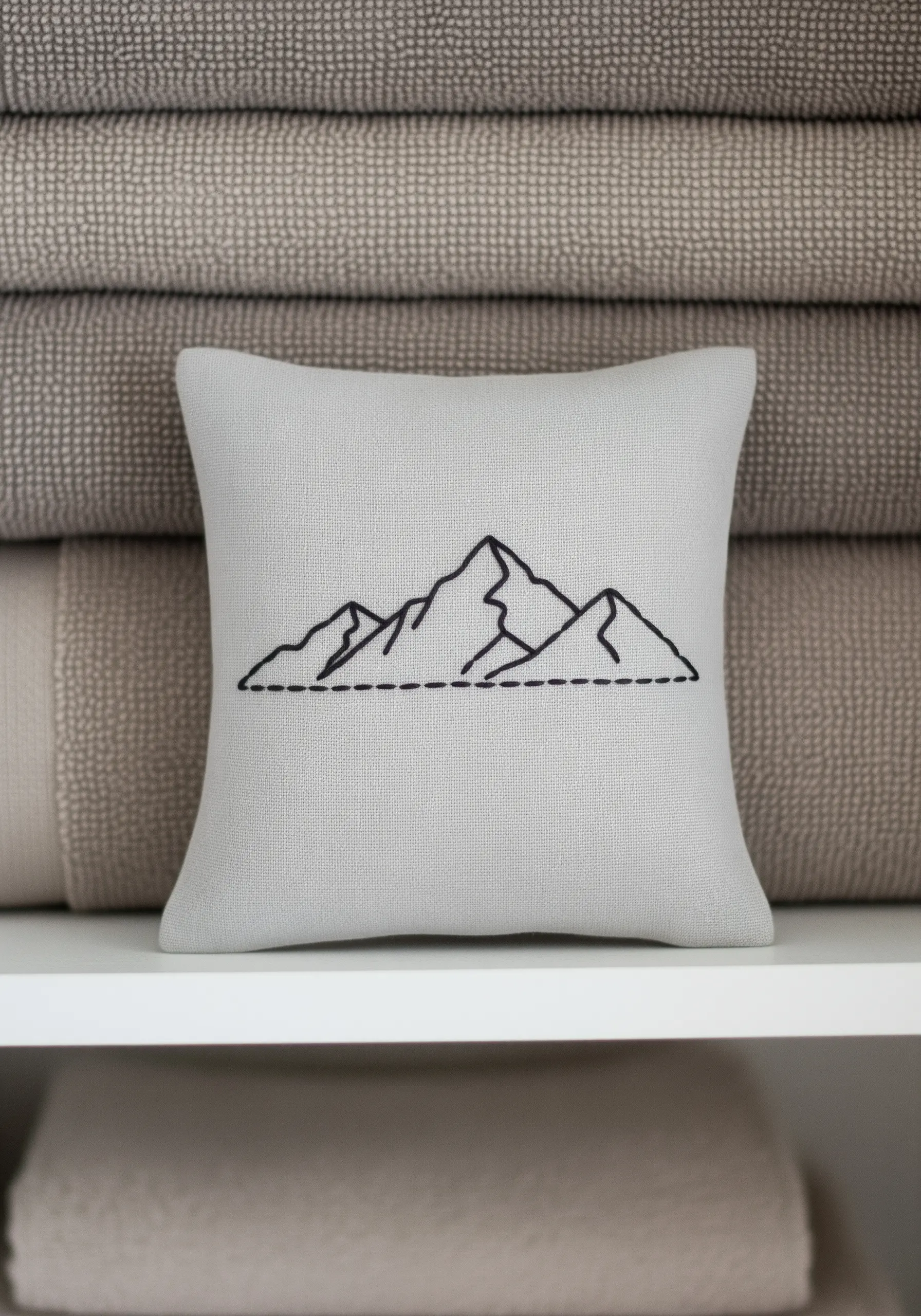 A minimalist black outline of a mountain range on a light gray throw pillow