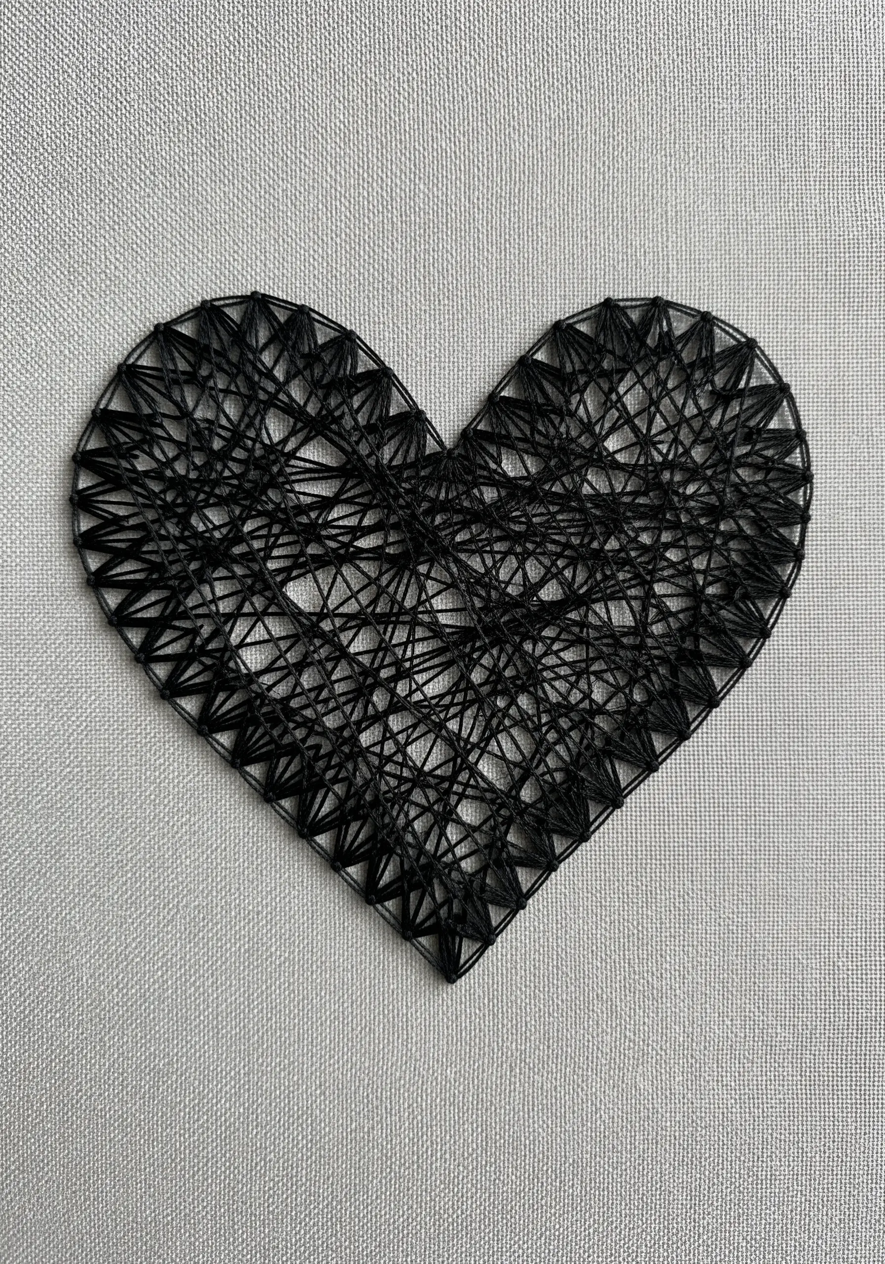 A minimalist heart created with a dense, chaotic web of black thread on white fabric.