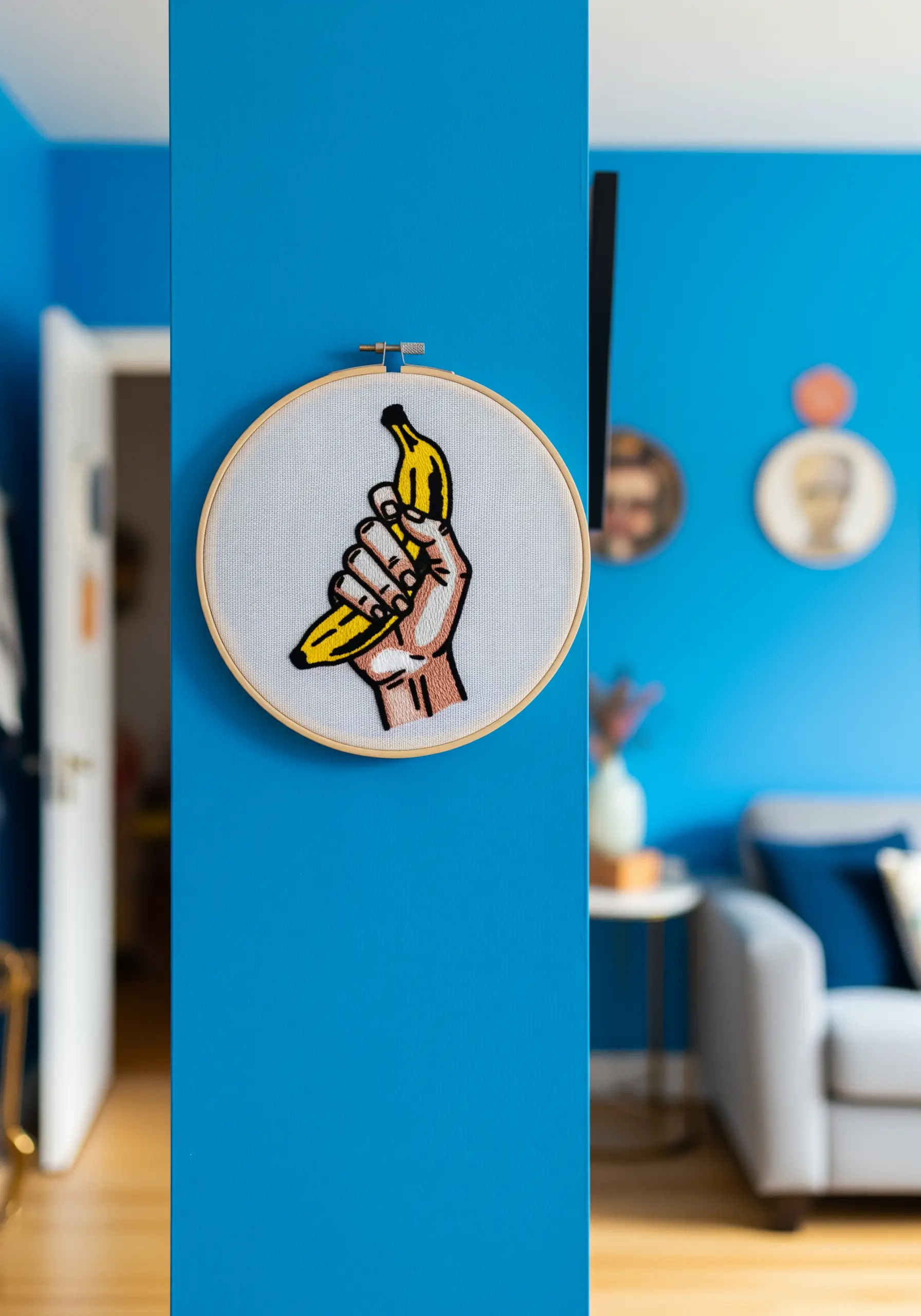 A Pop Art-style embroidery of a hand holding a banana against a bright blue wall.