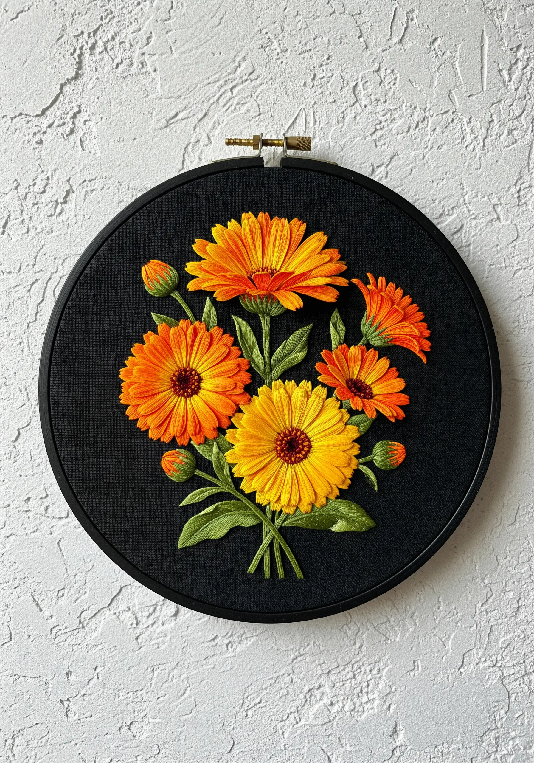 A vibrant bouquet of orange and yellow calendula flowers embroidered on black fabric in a black hoop.