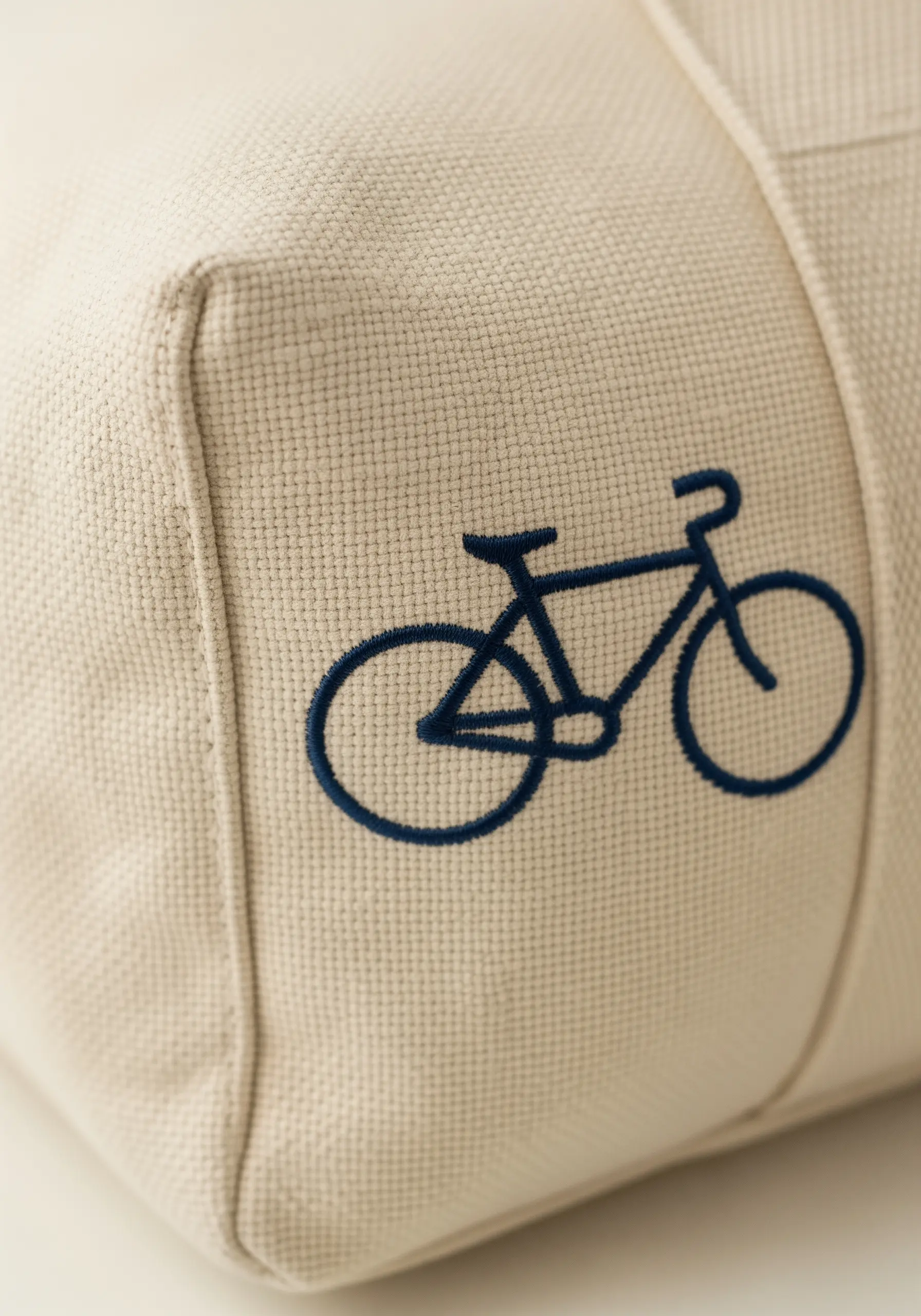 A minimalist bicycle outline embroidered in thick navy blue thread on a canvas tote.