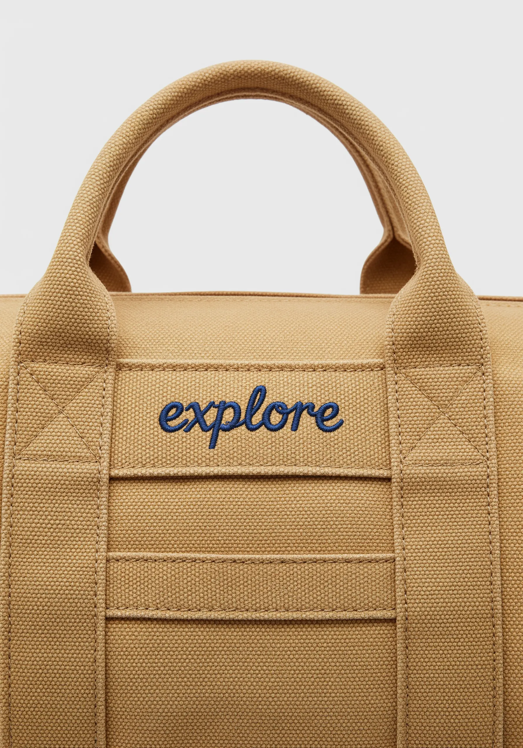 The word 'explore' embroidered in raised navy blue satin stitch on a tan canvas duffel bag.
