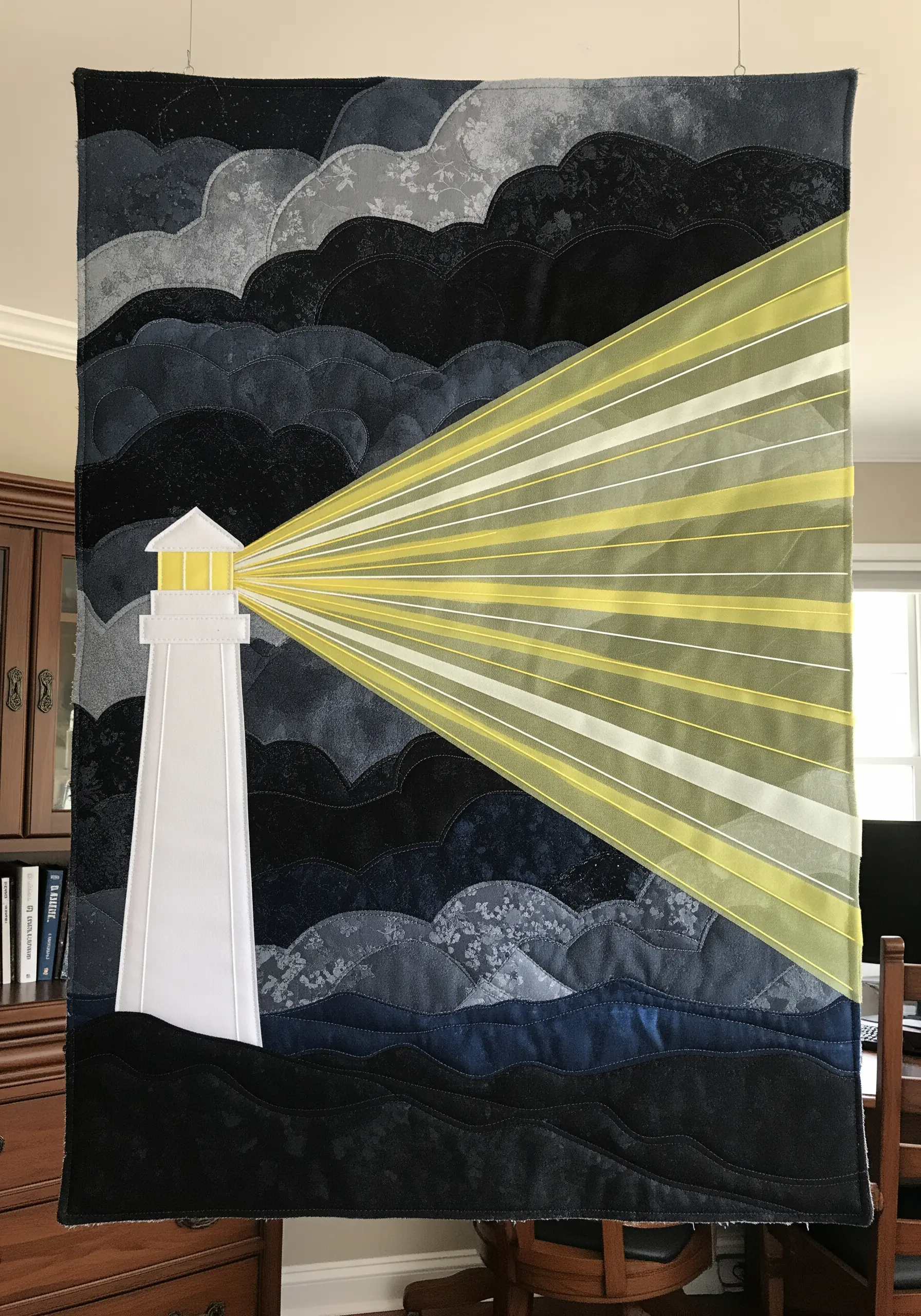 A fabric collage quilt of a lighthouse with beams of light made from layered sheer yellow fabric.
