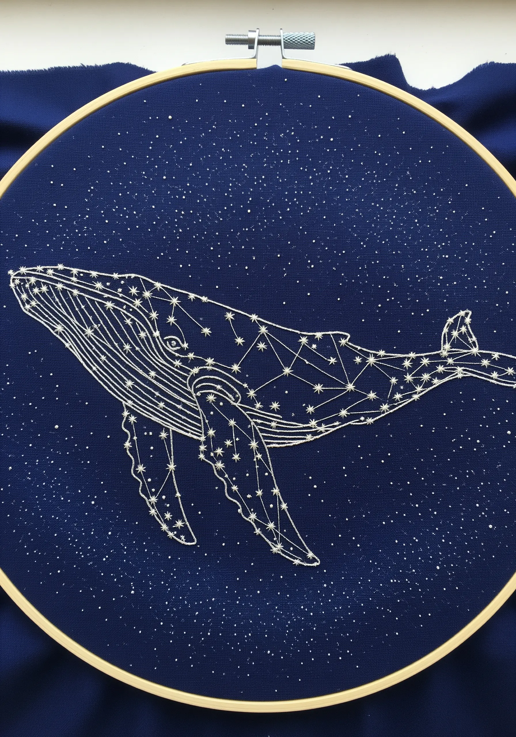 A whale embroidered as a constellation with white thread on dark blue fabric.