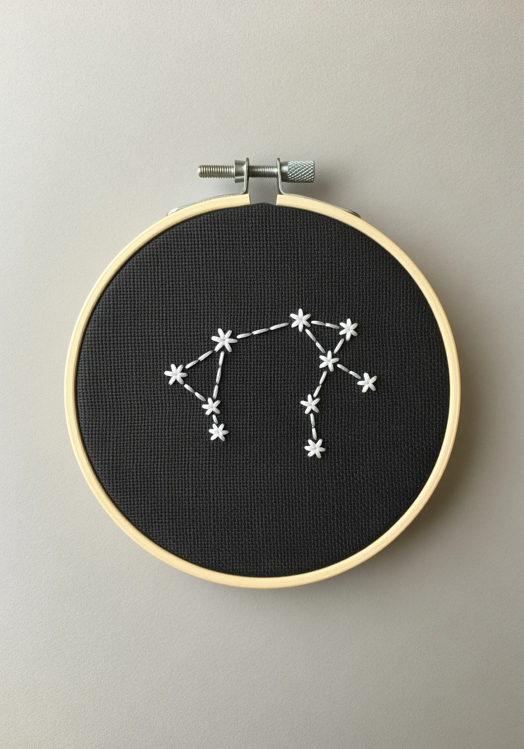 An embroidered Aquarius constellation with white thread on black fabric.