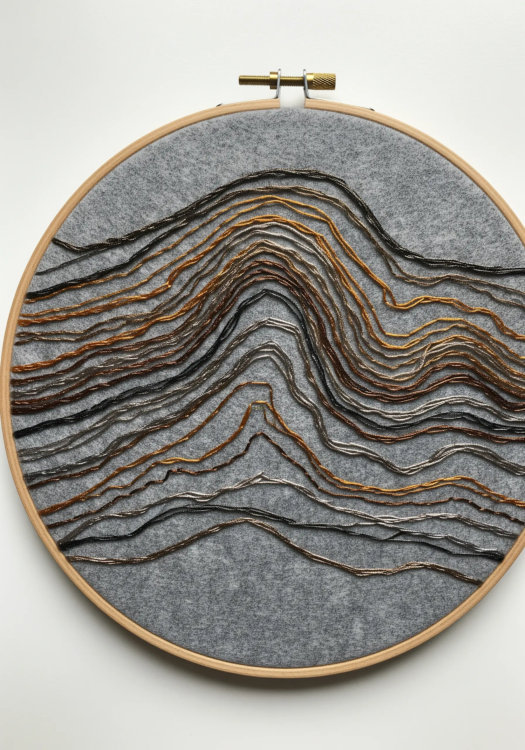 Topographical lines created with rows of metallic seed beads on gray felt in a hoop.